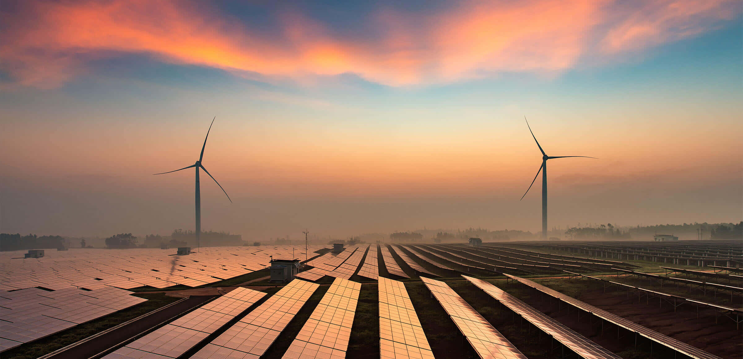 Wind 桌布 壁紙 — 一排排太陽能板在火紅的夕陽天空下向地平線延伸，遠處有兩座風力發電機高聳矗立。