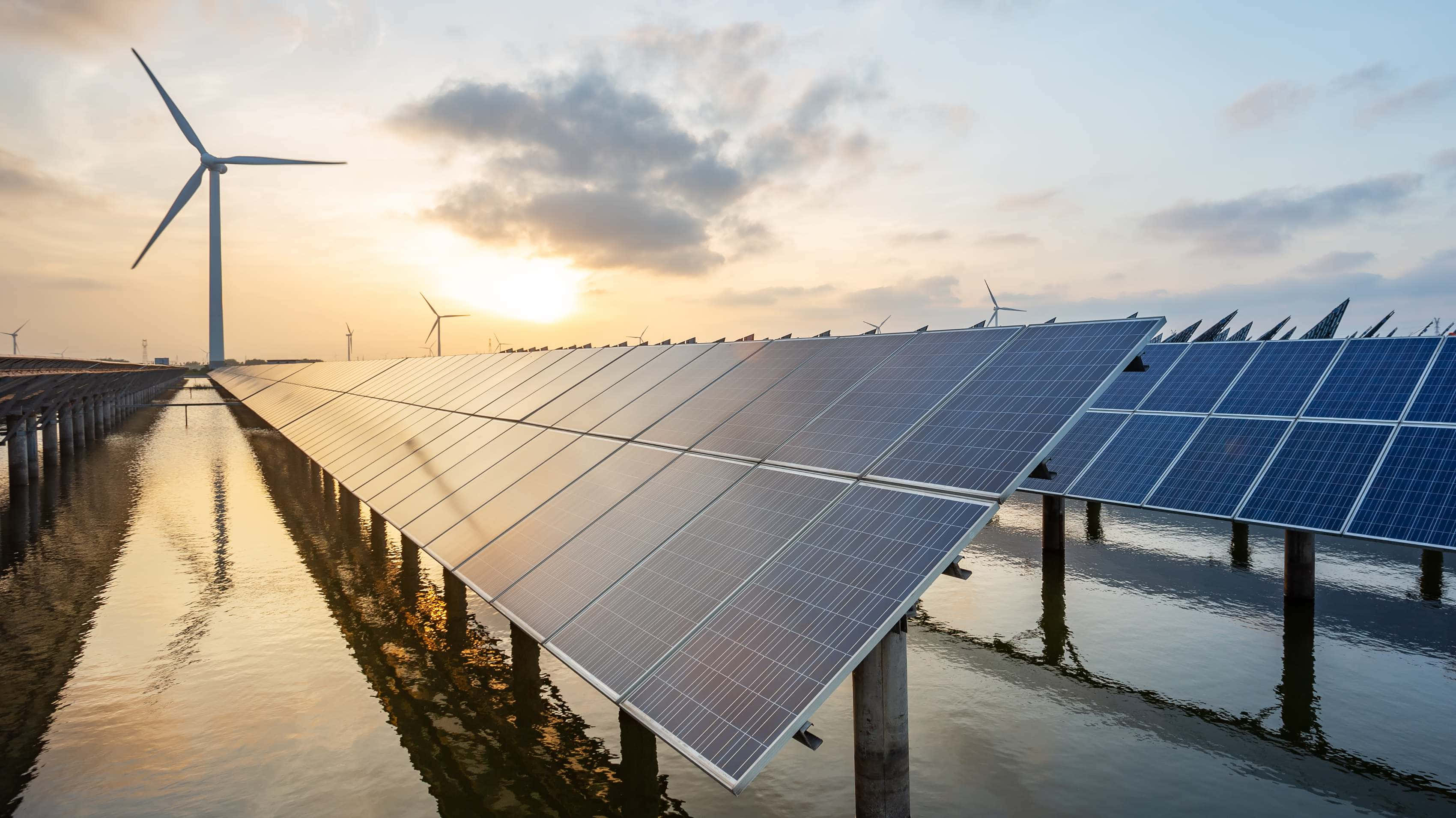Energy 桌布 壁紙 — 一排排太陽能板漂浮在水面上，風力渦輪機在金色夕陽天空下高高聳立。
