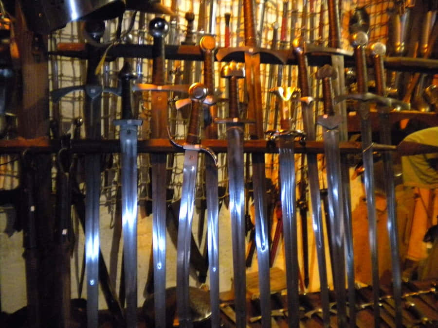 Ancient Weapons 桌布 壁紙 — 一排排帶有反光刀片的中世紀劍垂直懸掛在光線昏暗、溫暖的展示櫃中。