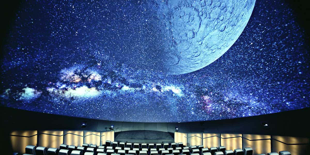Planetarium 桌布 壁紙 — 一排排座位面向一個彎曲的圓頂，顯示出明亮的星空，有一個大月亮和發光的星系。