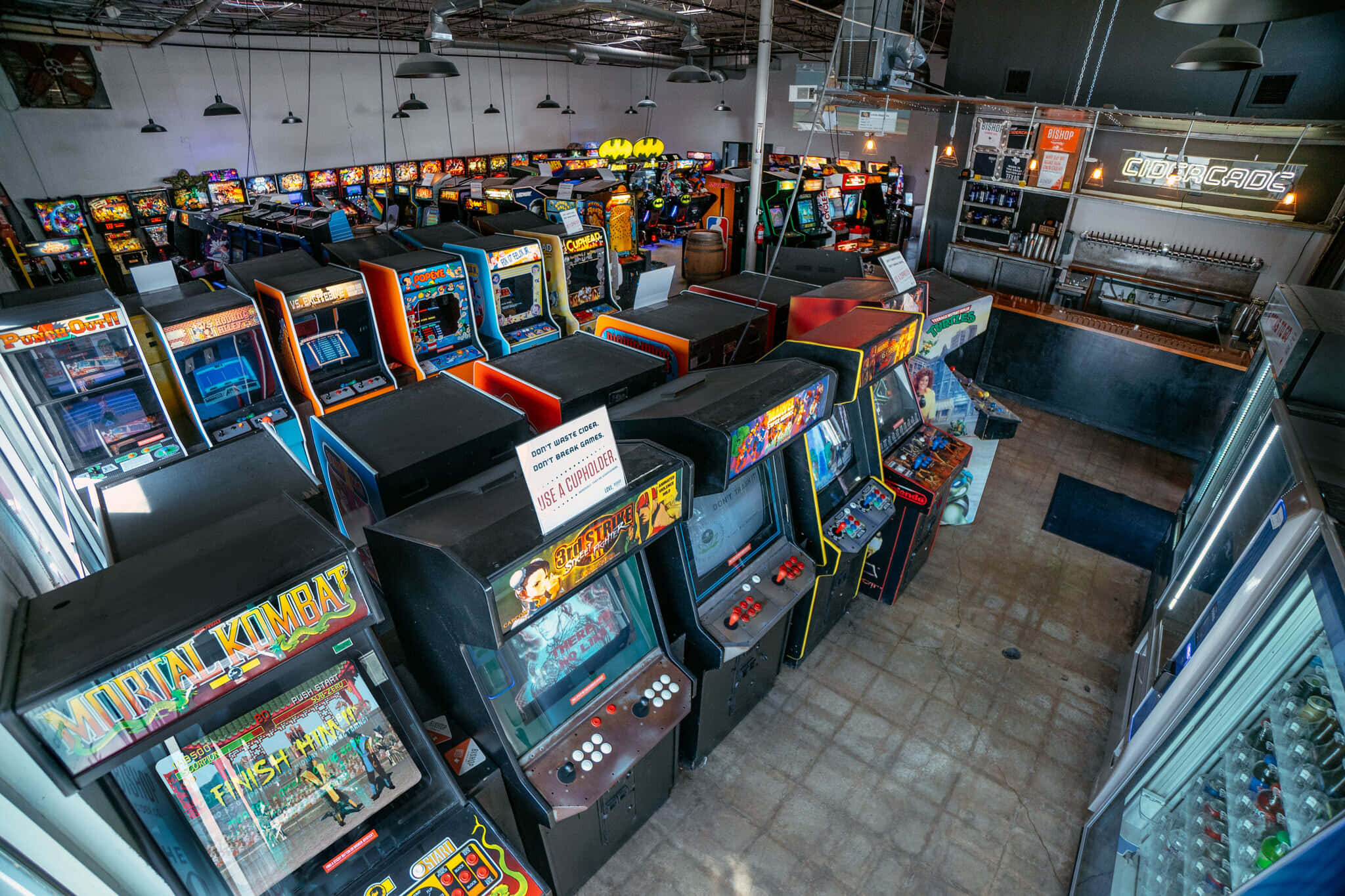 Arcade Games 桌布 壁紙 — 一排排復古街機，帶有發光屏幕和色彩繽紛的機櫃，在裸露的天花燈光下充滿了復古遊戲廳。