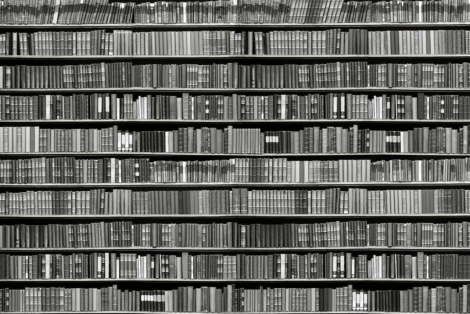 Black And White Book 桌布 壁紙 — 一排排書籍填滿單色圖書館中的高聳書架，營造出書脊與陰影的紋理圖案。