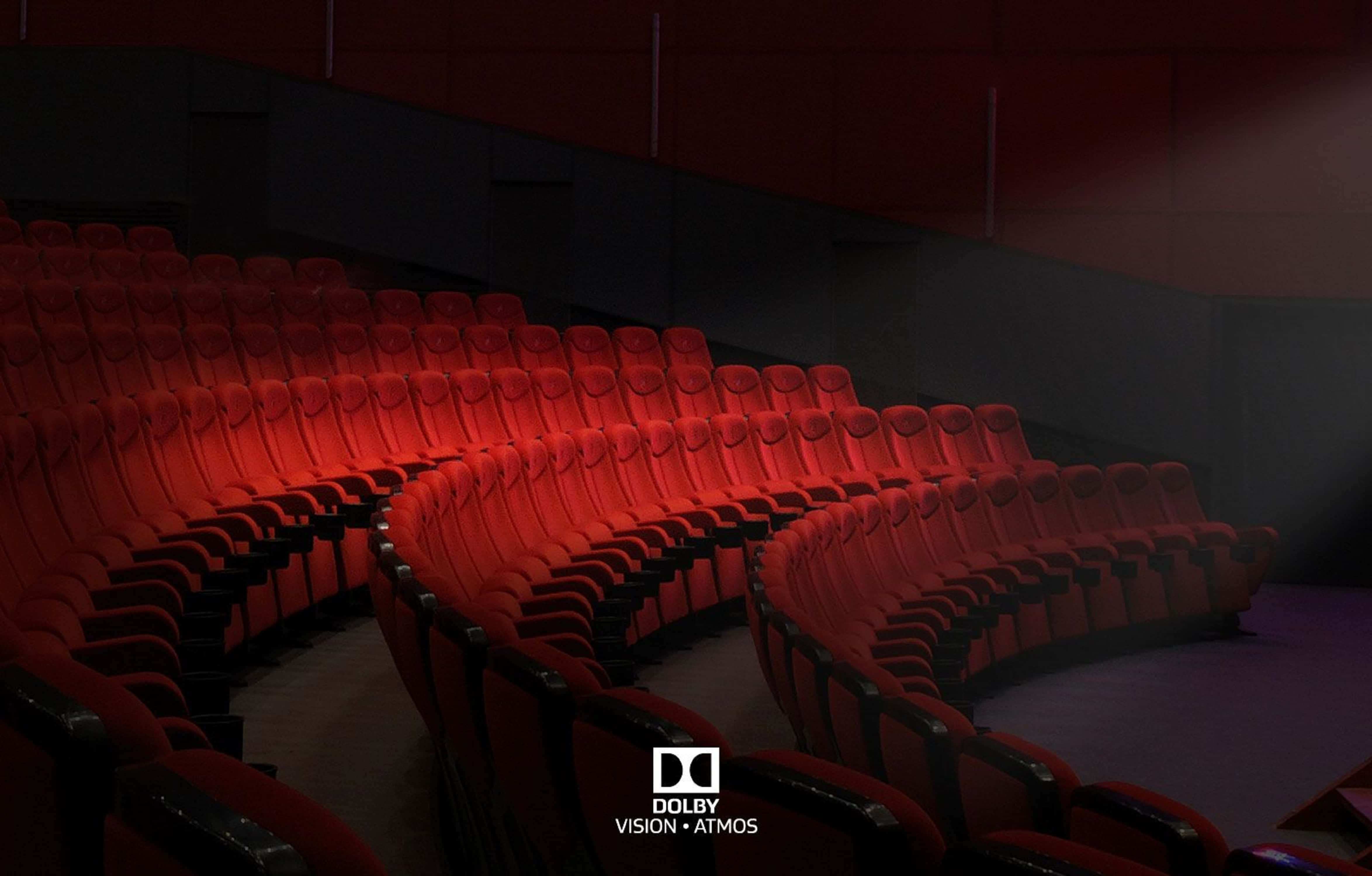 4K Dolby Vision 桌布 壁紙 — 一排排柔軟的紅色電影院座椅在昏暗的影院中向上彎曲，沐浴在環境紅光中。