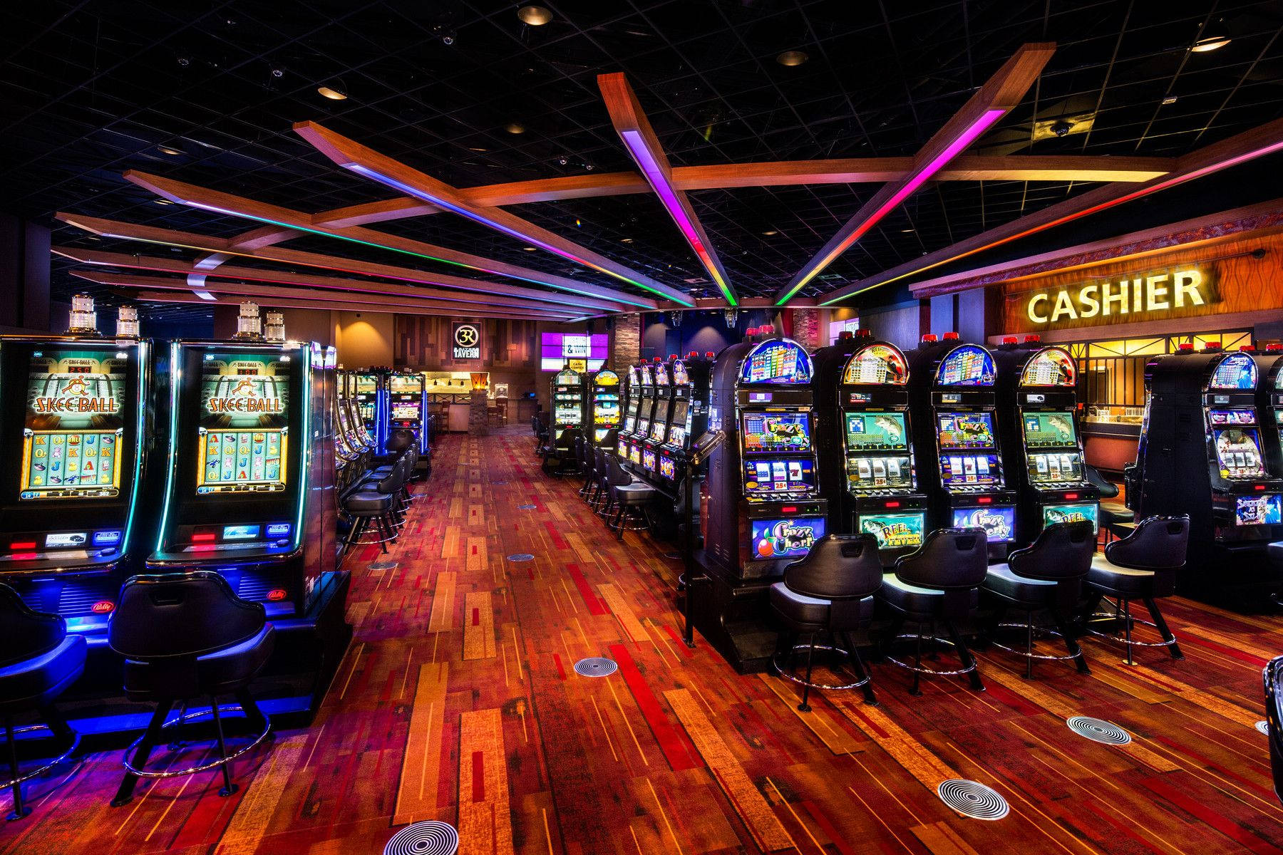 Keno Arcade Machines In Casino 壁紙 — 一排排發光的角子機排列在充滿活力的賭場地板上，腳下是色彩繽紛的霓虹燈和拋光的木板。