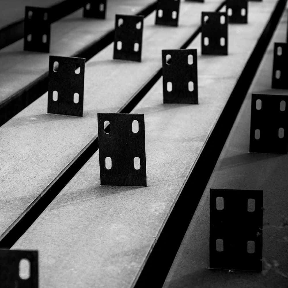 Domino 桌布 壁紙 — 一排排相同的黑色金屬支架帶有孔洞，整齊地排列在單色紋理工業表面上。