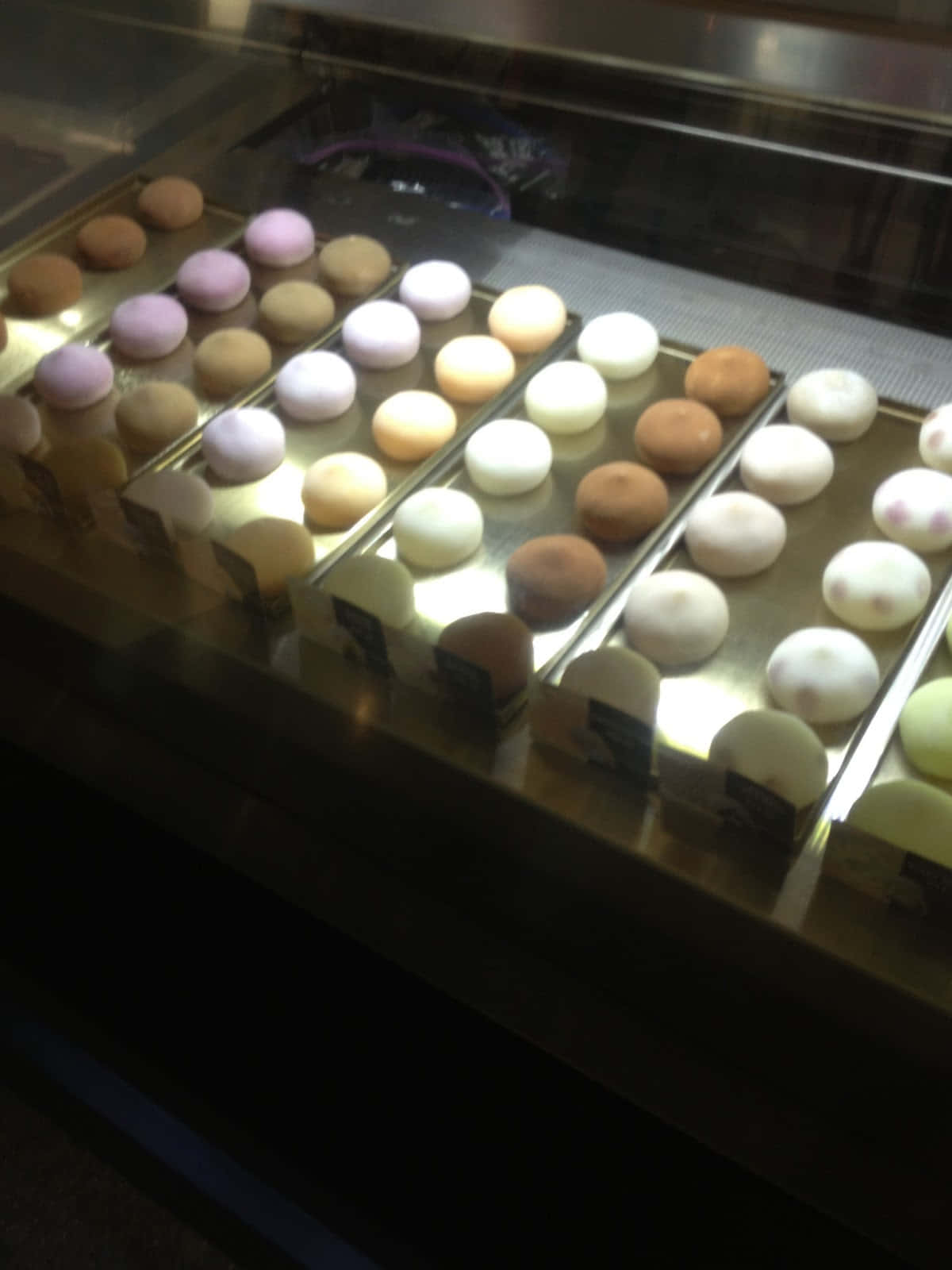 Japanese Sweets 桌布 壁紙 — 一排排粉彩色和白色的馬卡龍整齊地排列在暖光下的玻璃展示櫃中。