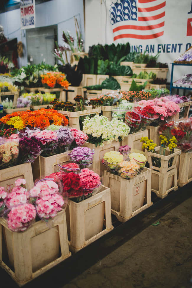 Flower Market 桌布 壁紙 — 一排排色彩繽紛的花束放在木箱中，充滿了美國國旗下的熱鬧室內市場。