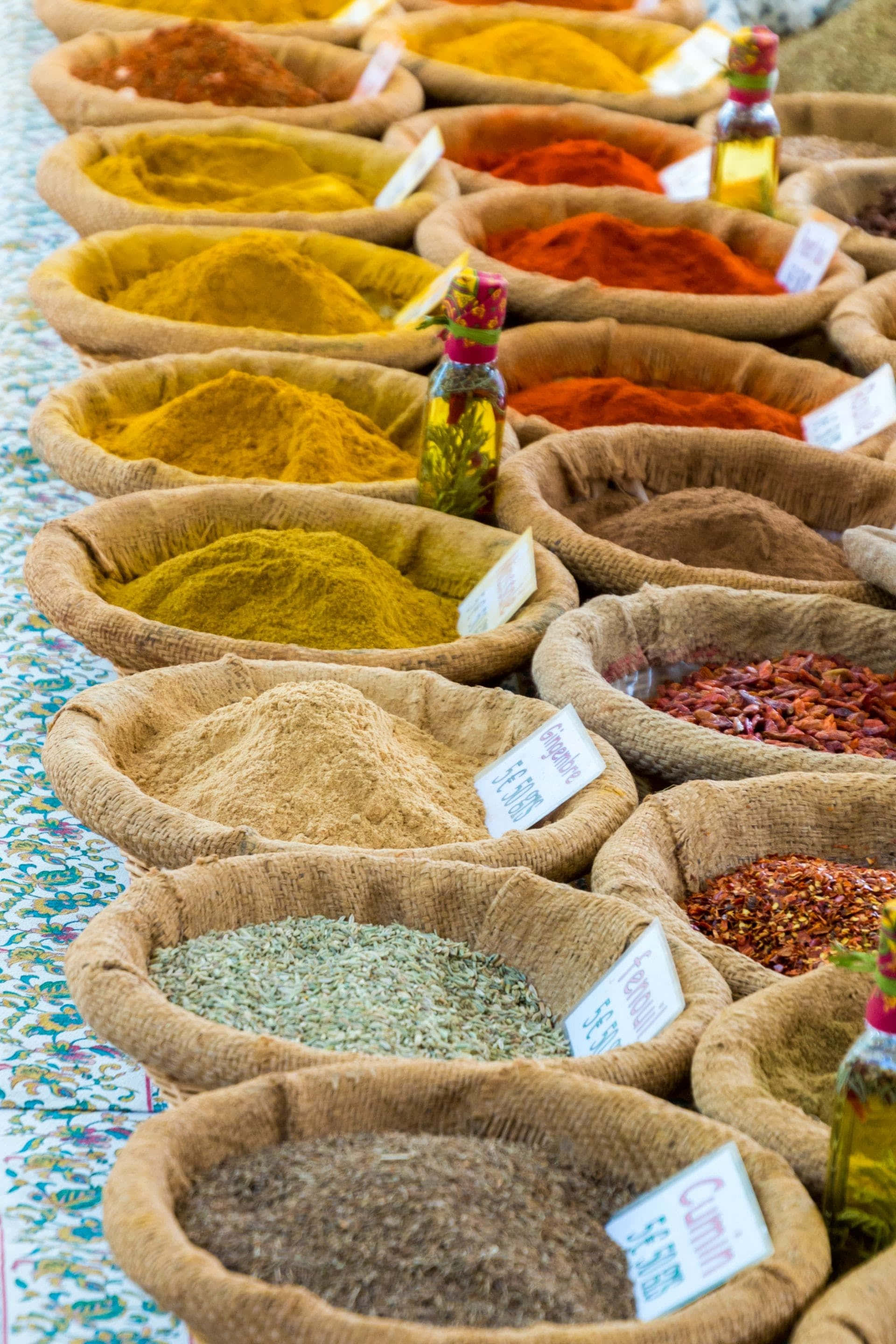 Spice 桌布 壁紙 — 一排排裝在麻布袋中的鮮豔香料，在熙熙攘攘的市場攤位上展現出火紅、黃色和大地棕色。