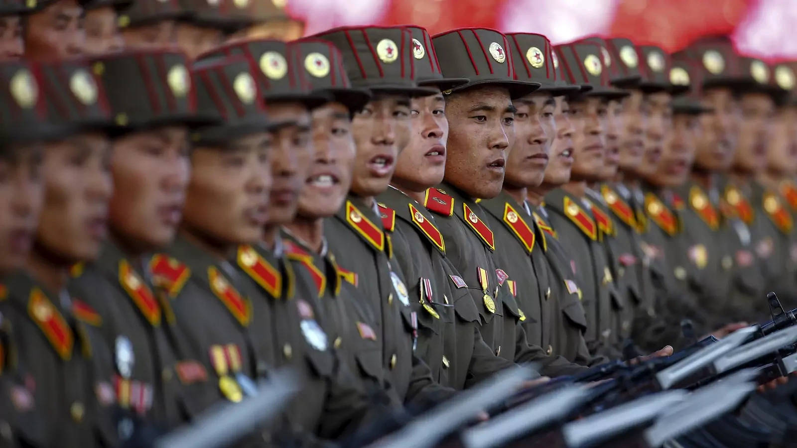 North Korea 桌布 壁紙 — 一排排身穿橄欖綠制服、戴著紅邊帽子的士兵，整齊劃一地持槍立正。