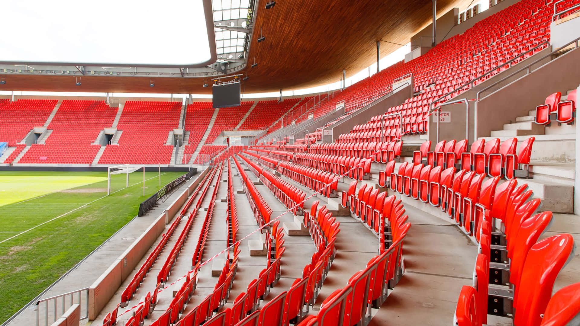 Soccer Stadium 桌布 壁紙 — 一排排鮮紅色的體育場座位向上彎曲，朝向木質天花板，俯瞰著鬱鬱蔥蔥的綠色足球場。