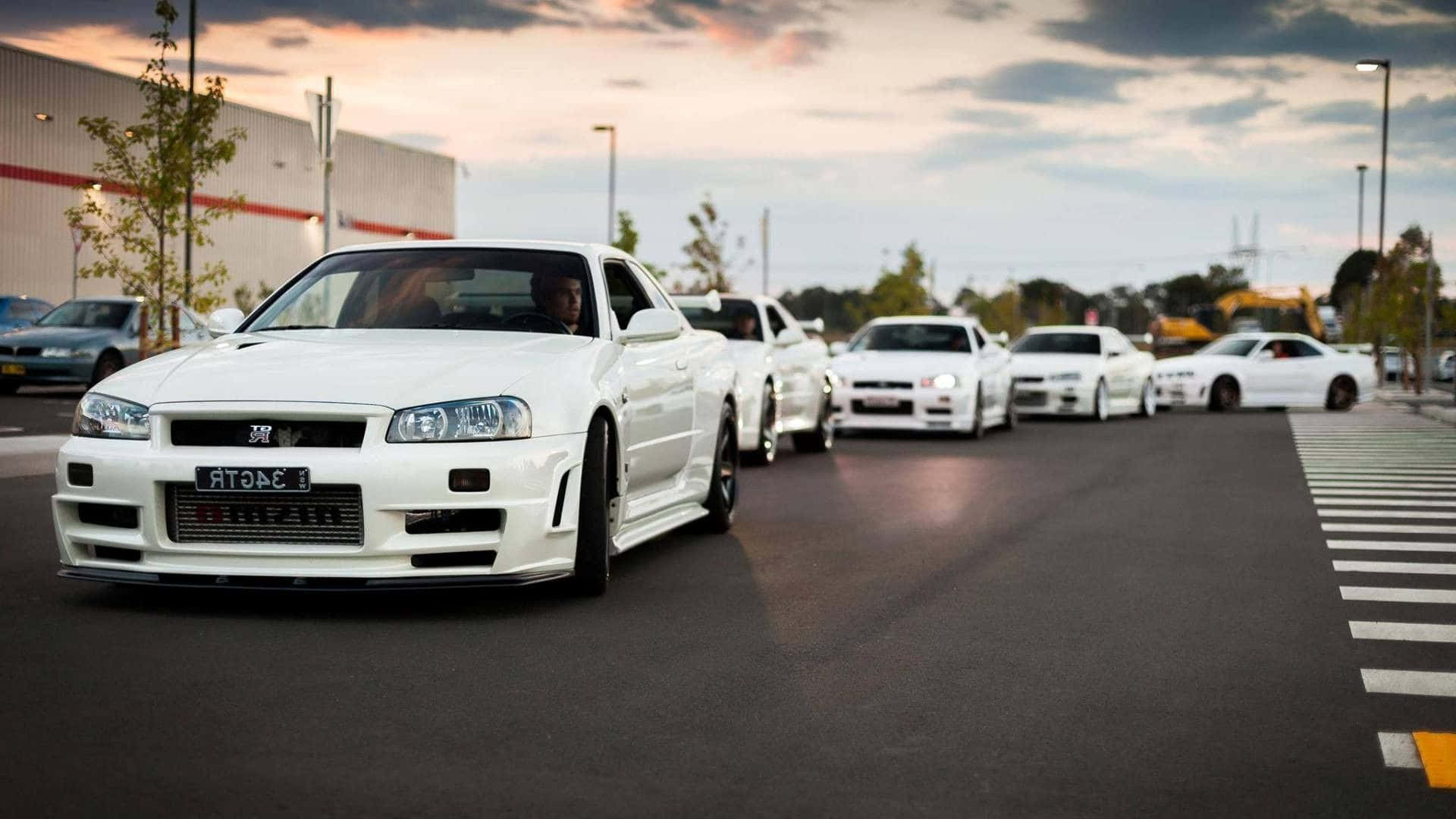 JDM 車 桌布 壁紙 — 一排白色日產Skyline GT-R停泊在瀝青場地上，天空多雲，暮色蒼茫。