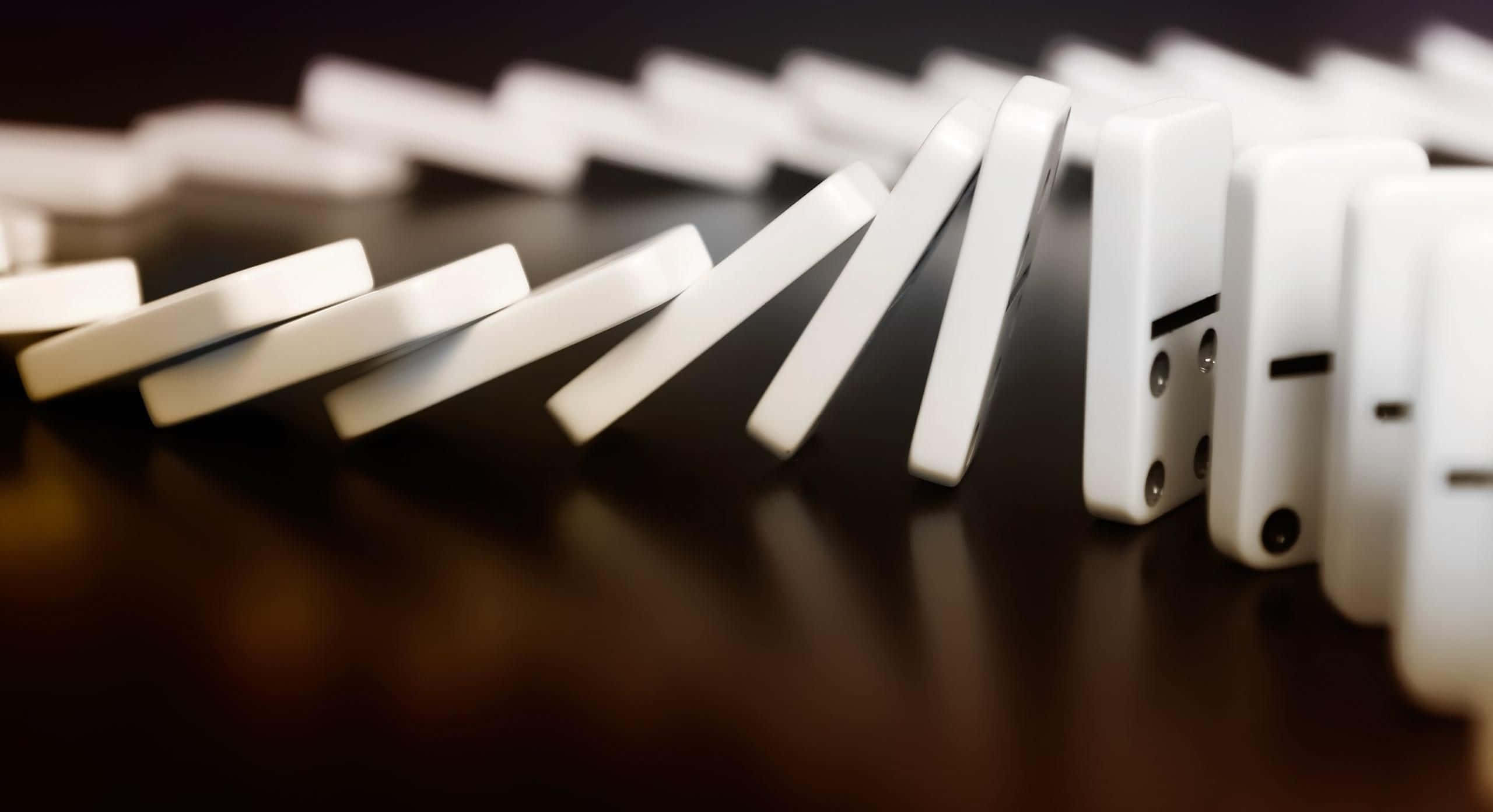 Domino 桌布 壁紙 — 一排白色骨牌在深色反光表面上以慢動作倒下，營造出無可避免的連鎖反應感。