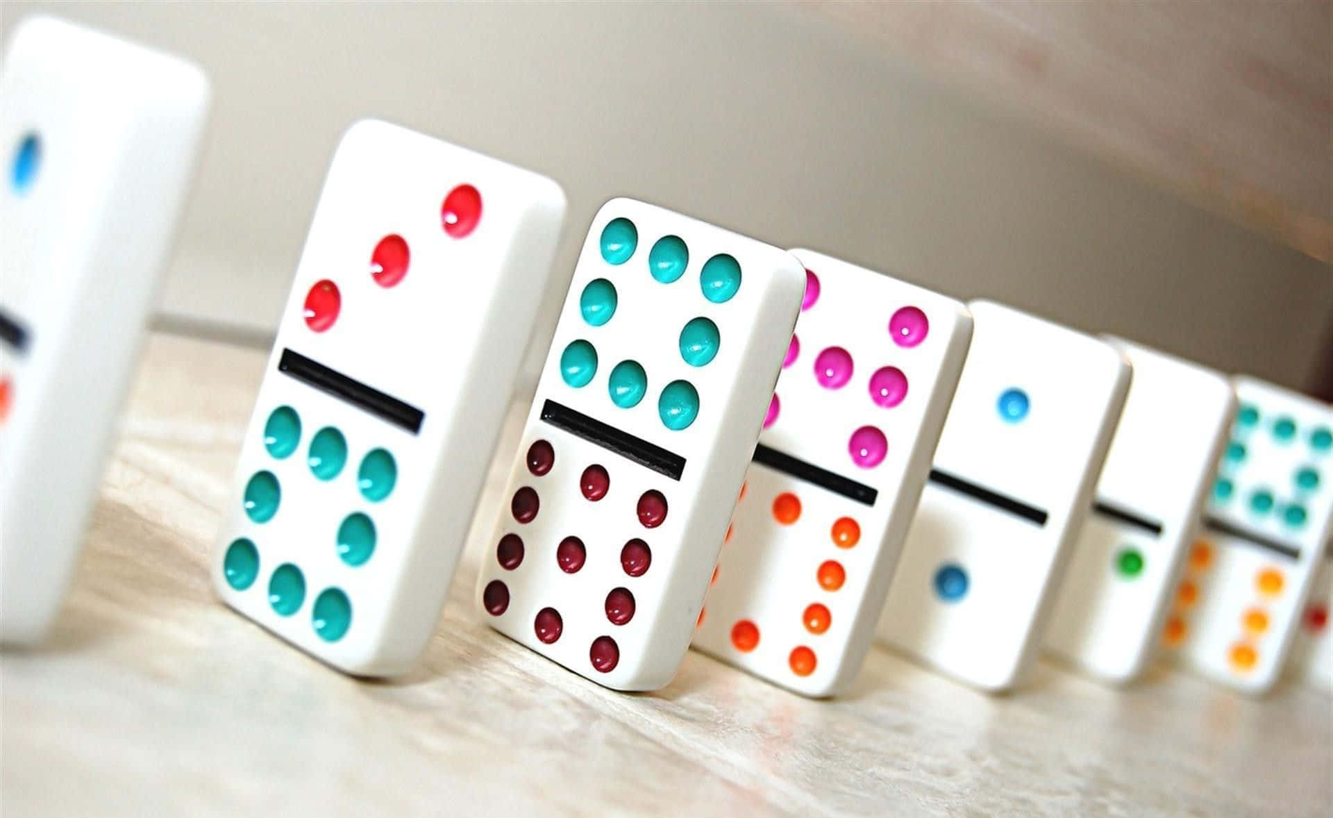 Domino 桌布 壁紙 — 一排色彩繽紛的骨牌，帶有紅色、藍綠色、粉紅色和橙色的圓點，直立於淺色木質表面上。