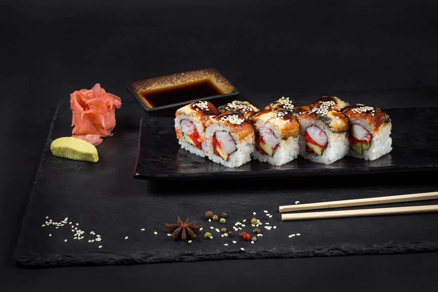 Sushi 桌布 壁紙 — 一排酥脆的天婦羅壽司卷撒上芝麻，放在黑色石板盤上，旁邊有生薑芥末和醬油。