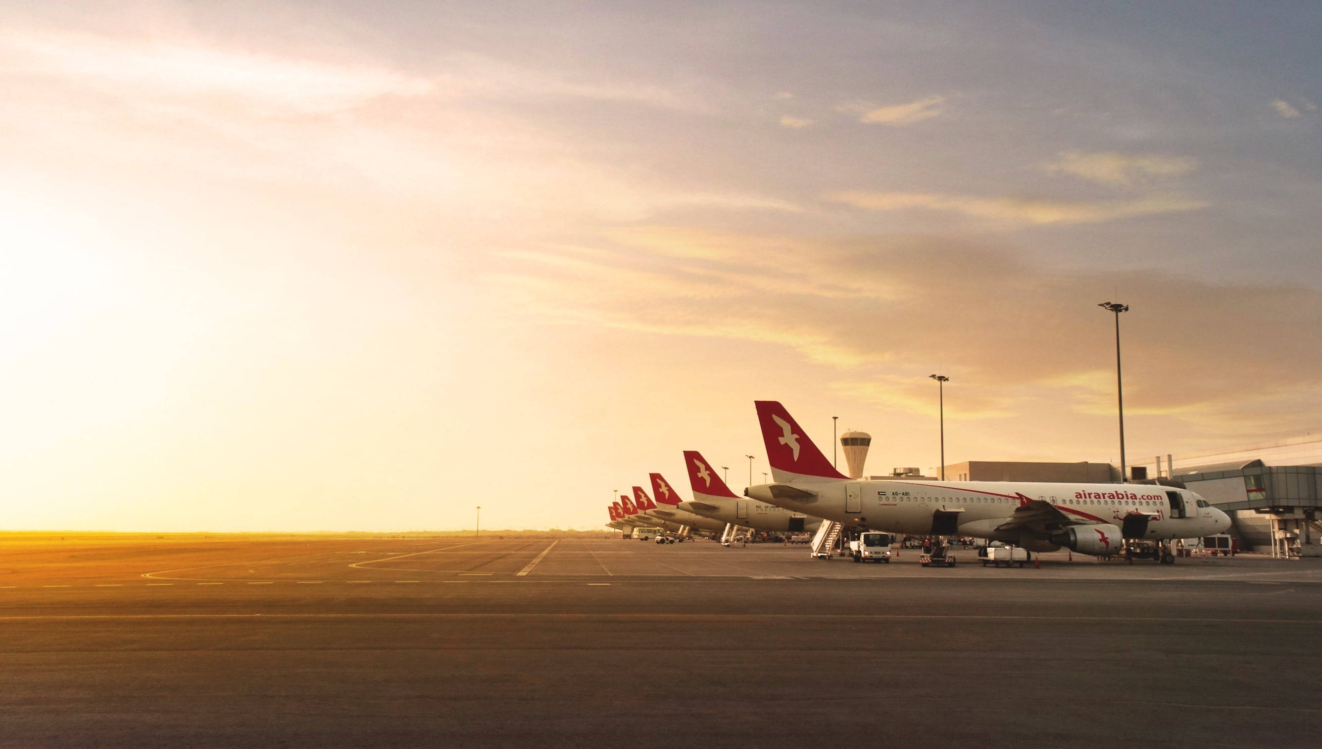 Airport 桌布 壁紙 — 一排阿拉伯航空飛機停泊在機場客運大樓，沐浴在夕陽溫暖的金色光芒中。