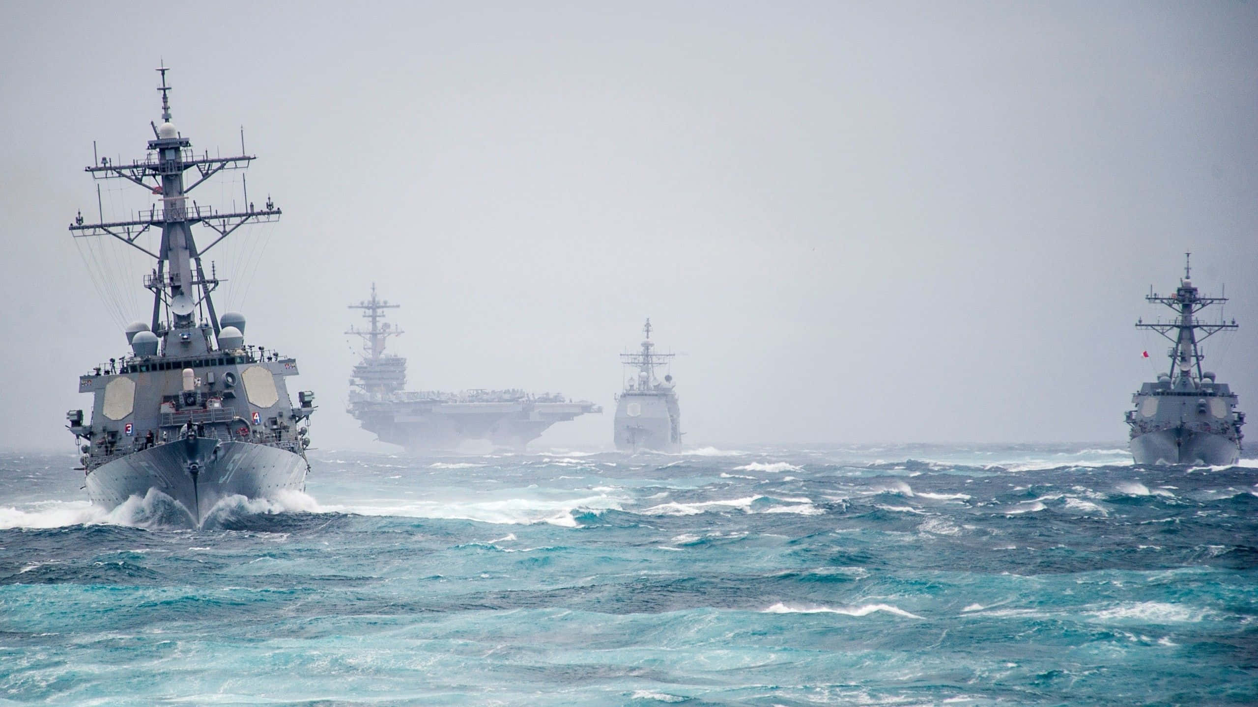 Navy 桌布 壁紙 — 一支包括航空母艦在內的海軍艦隊，在陰天之下穿越波濤洶湧的碧綠海水。