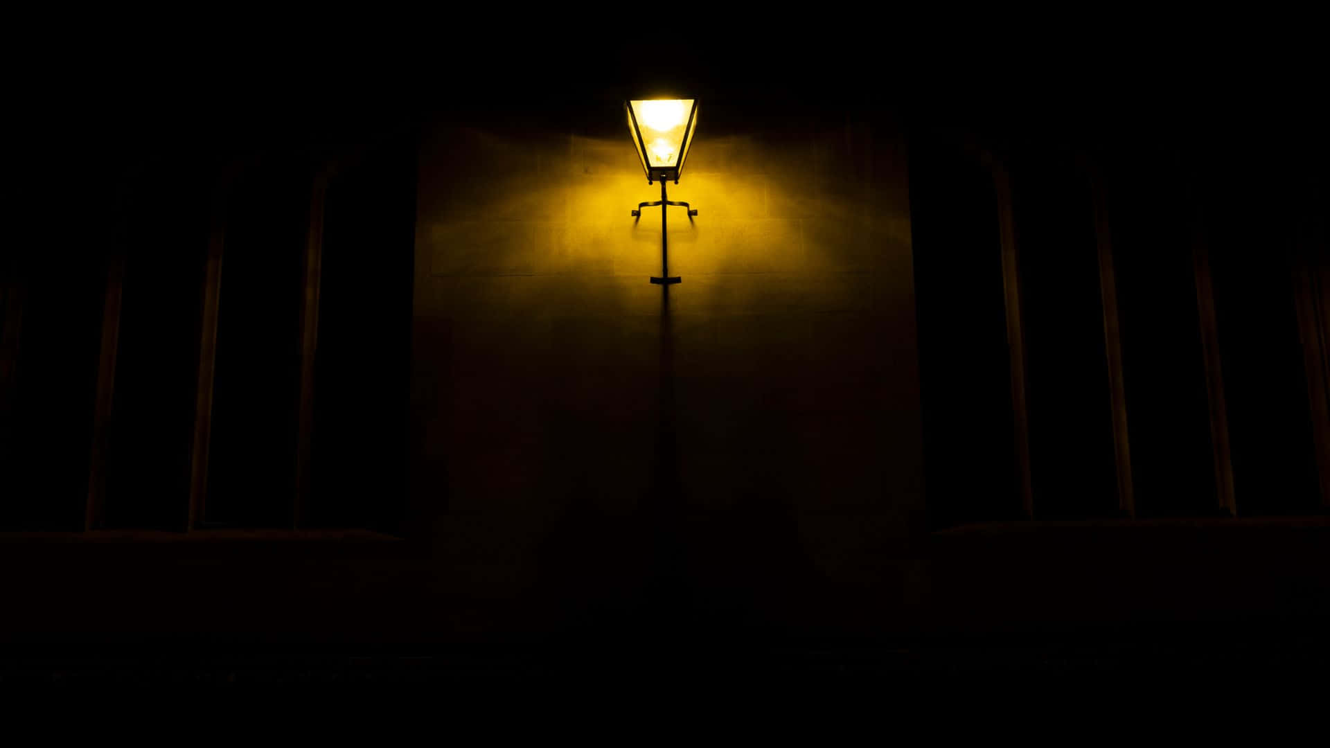 Dark Night 桌布 壁紙 — 一支復古街燈在夜晚空無一人的城市小巷中，向黑暗的牆壁投射出溫暖的金色光芒。