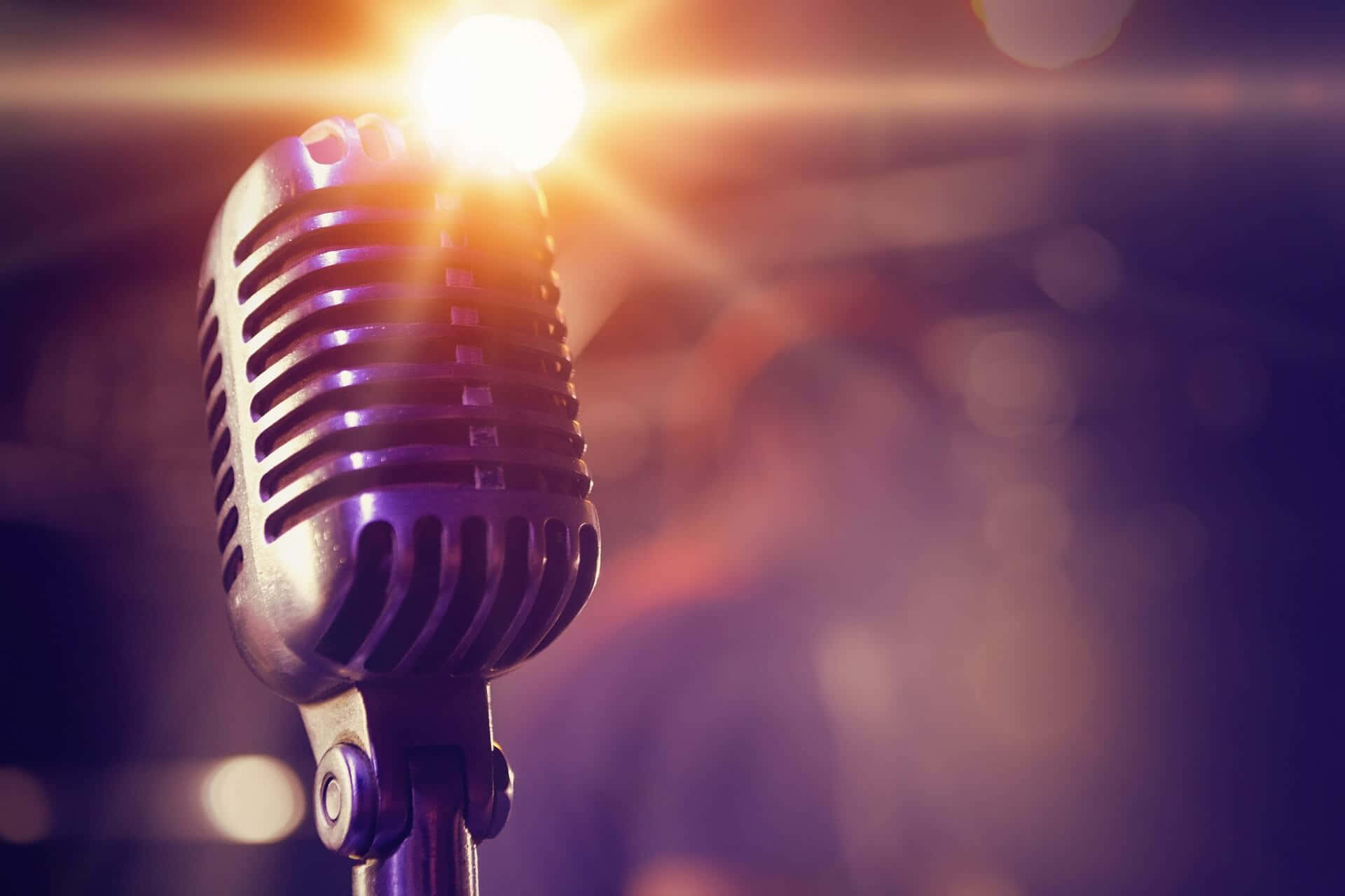 Microphone 桌布 壁紙 — 一支復古麥克風在明亮的聚光燈下閃耀，背景有溫暖的金色光線和紫色散景。
