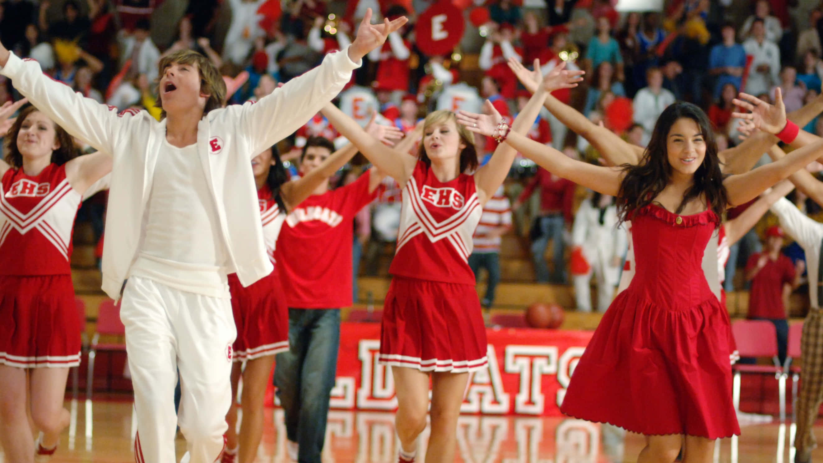 High School Musical 桌布 壁紙 — 一支穿著紅白制服的高中啦啦隊在體育館地板上充滿活力地表演，背景有群眾。