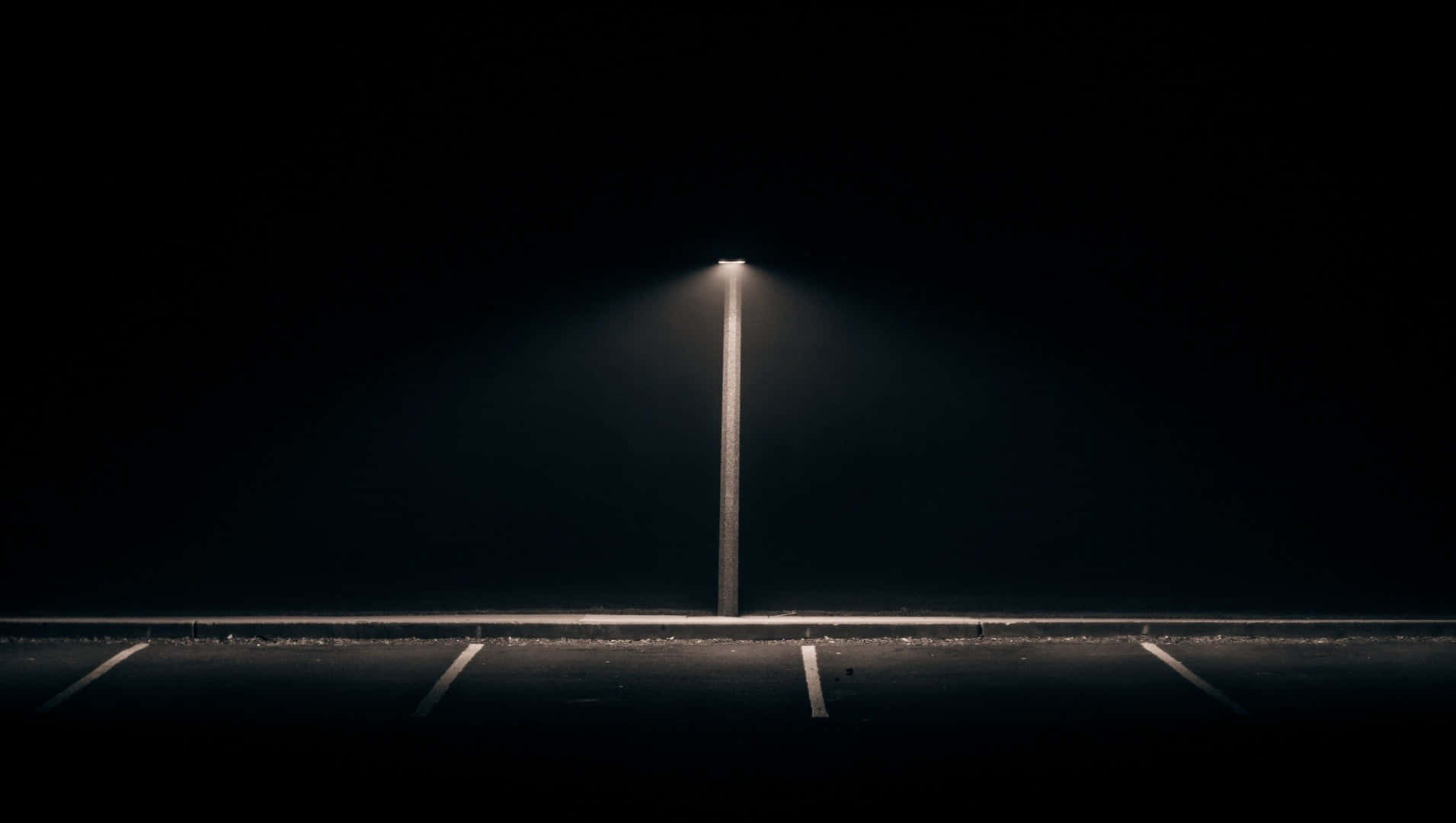 Dark Road 桌布 壁紙 — 一支街燈在漆黑一片的夜晚場景中，將一道狹窄的光束投射在空蕩蕩的停車位上。