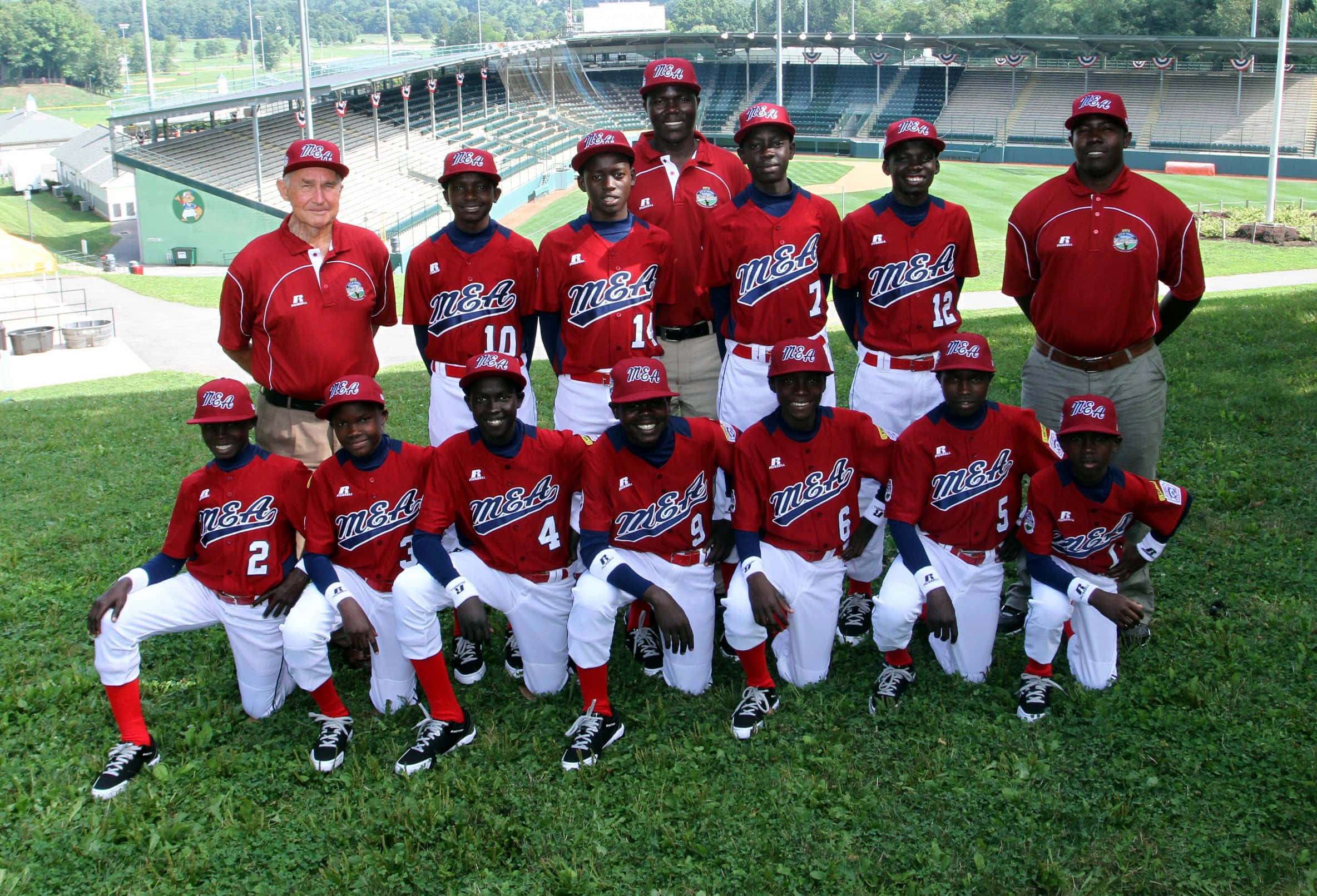 Little League Baseball 桌布 壁紙 — 一支身穿紅色球衣的青少年棒球隊在陽光明媚的球場上自豪地擺姿勢，背景是體育場看台。