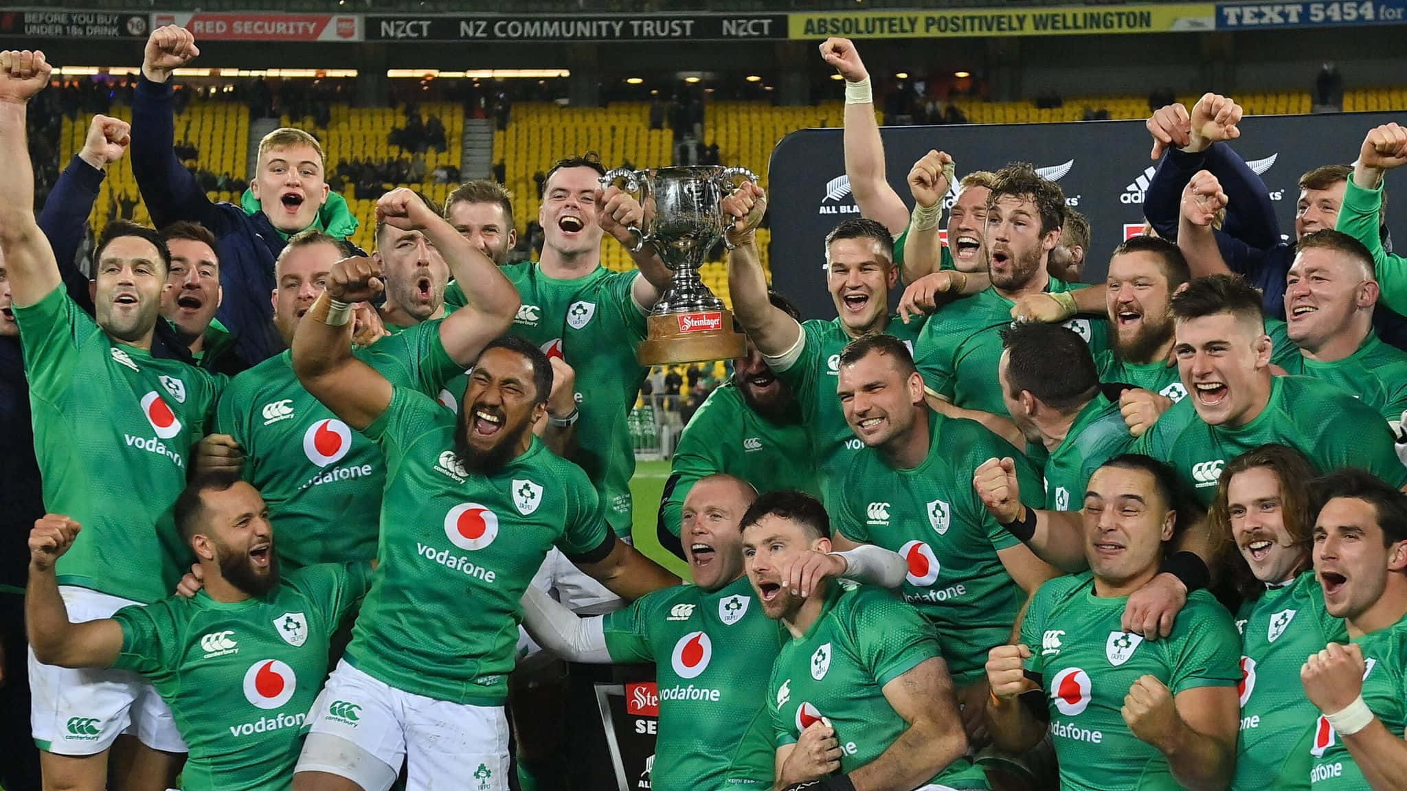 Ireland Rugby 桌布 壁紙 — 一支身穿綠色球衣的歡騰欖球隊在體育館內高舉閃亮的獎盃，拳頭高舉慶祝勝利。