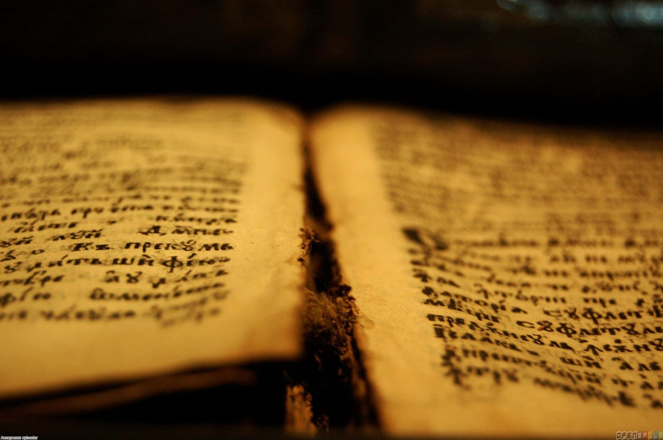 Bible Study 桌布 壁紙 — 一本古老的手寫書，泛黃的書頁和褪色的文字在昏暗的環境中被溫暖的光線照亮。
