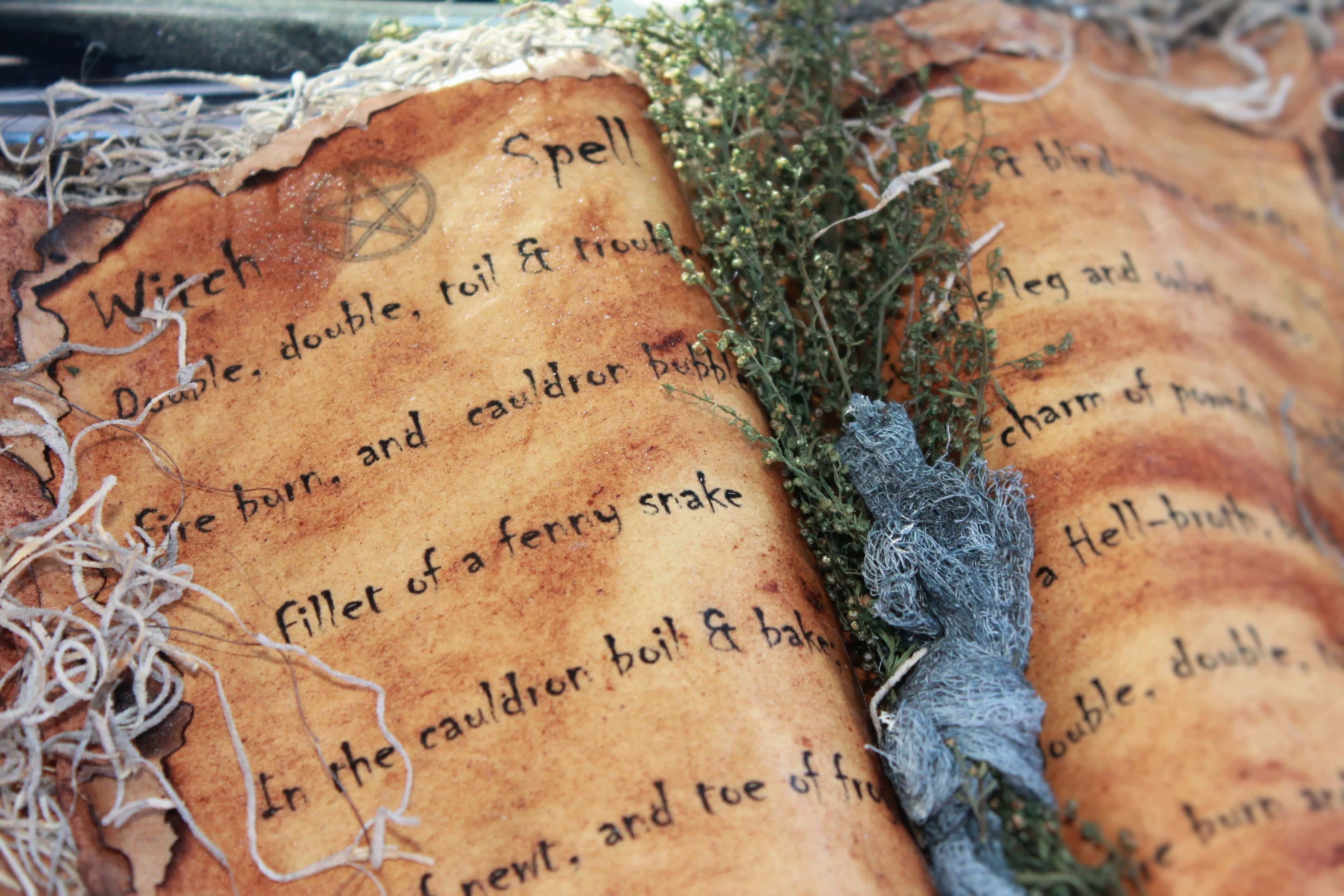 Grimoire 桌布 壁紙 — 一本古老的法術書，上面有手寫的咒語，打開放在乾燥草藥和繩子旁邊。