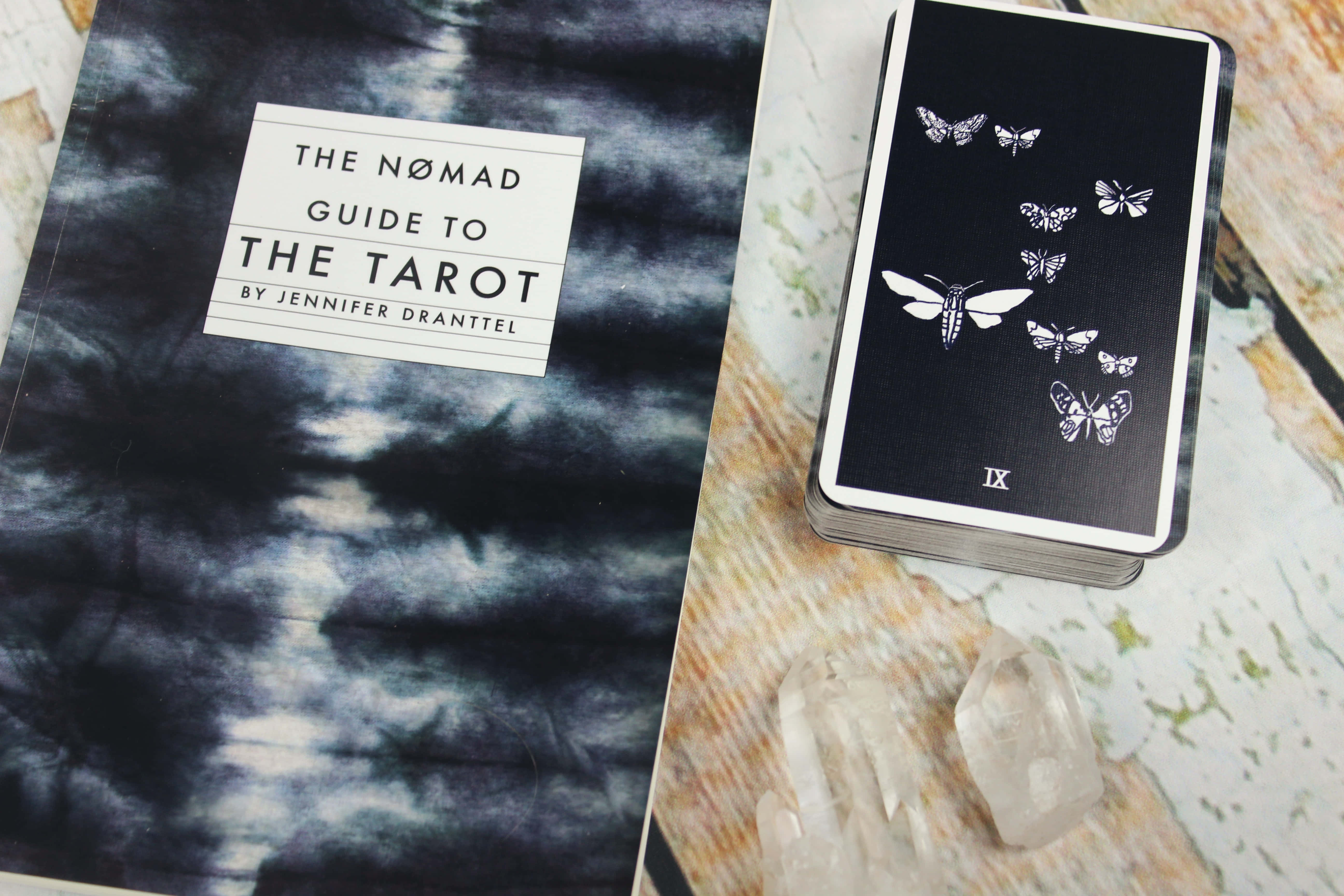Tarot Card 桌布 壁紙 — 一本塔羅書和蝴蝶主題牌組放在大理石紋理表面上的透明水晶旁邊。