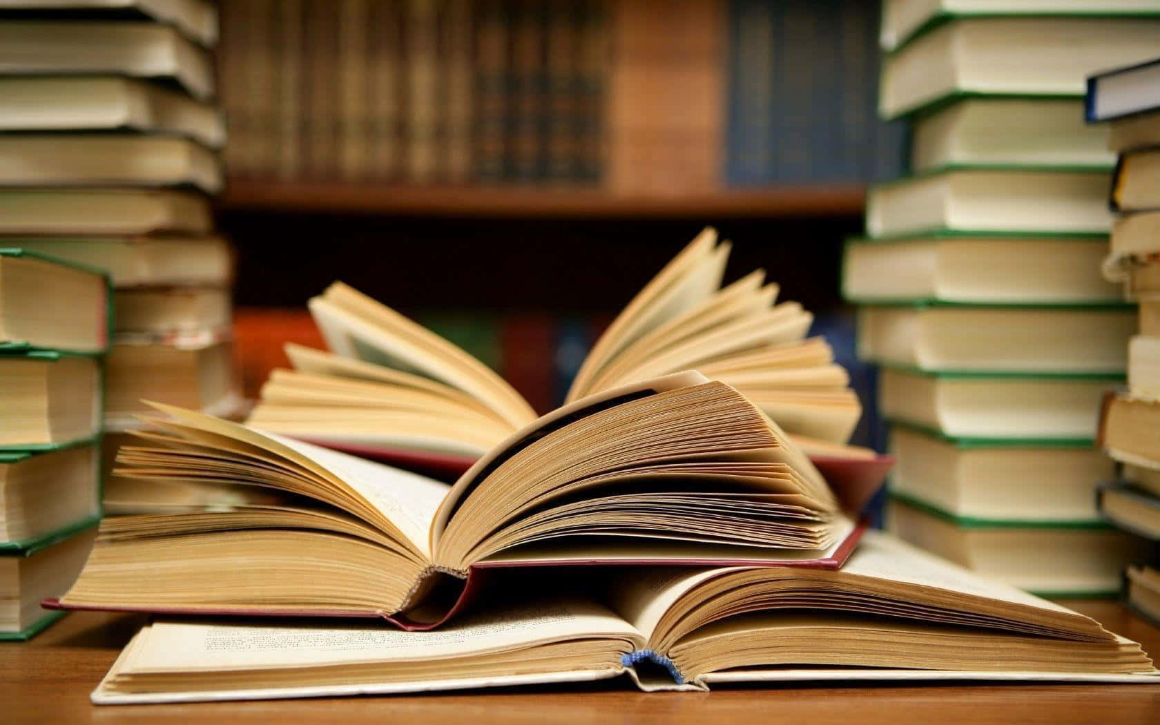 溫習 桌布 壁紙 — 一本打開的書放在木桌上，周圍是堆疊如山的書籍，營造出舒適的圖書館氛圍。