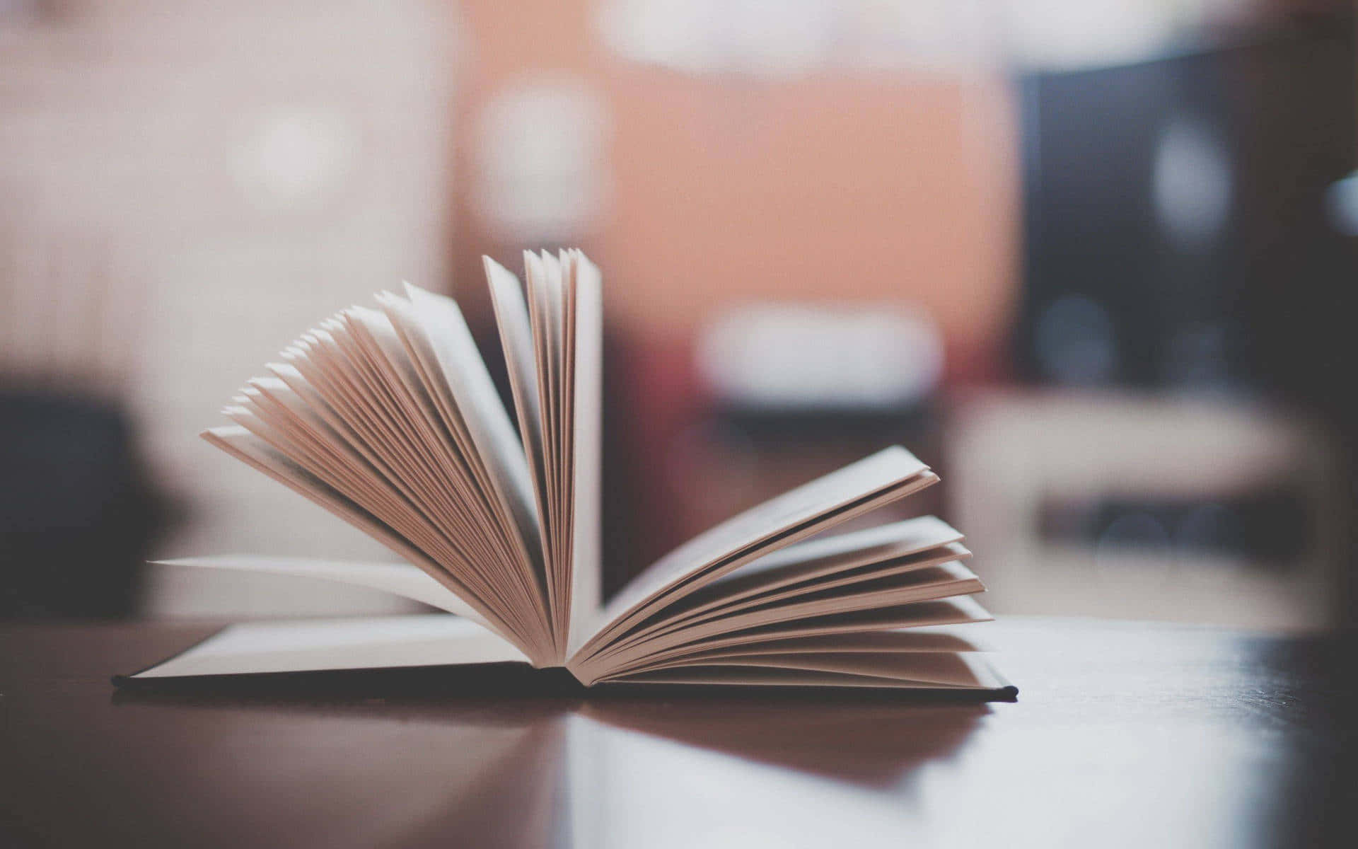 閱讀 桌布 壁紙 — 一本打開的書放在木質表面上，帶有柔和溫暖的燈光和模糊的背景家具。