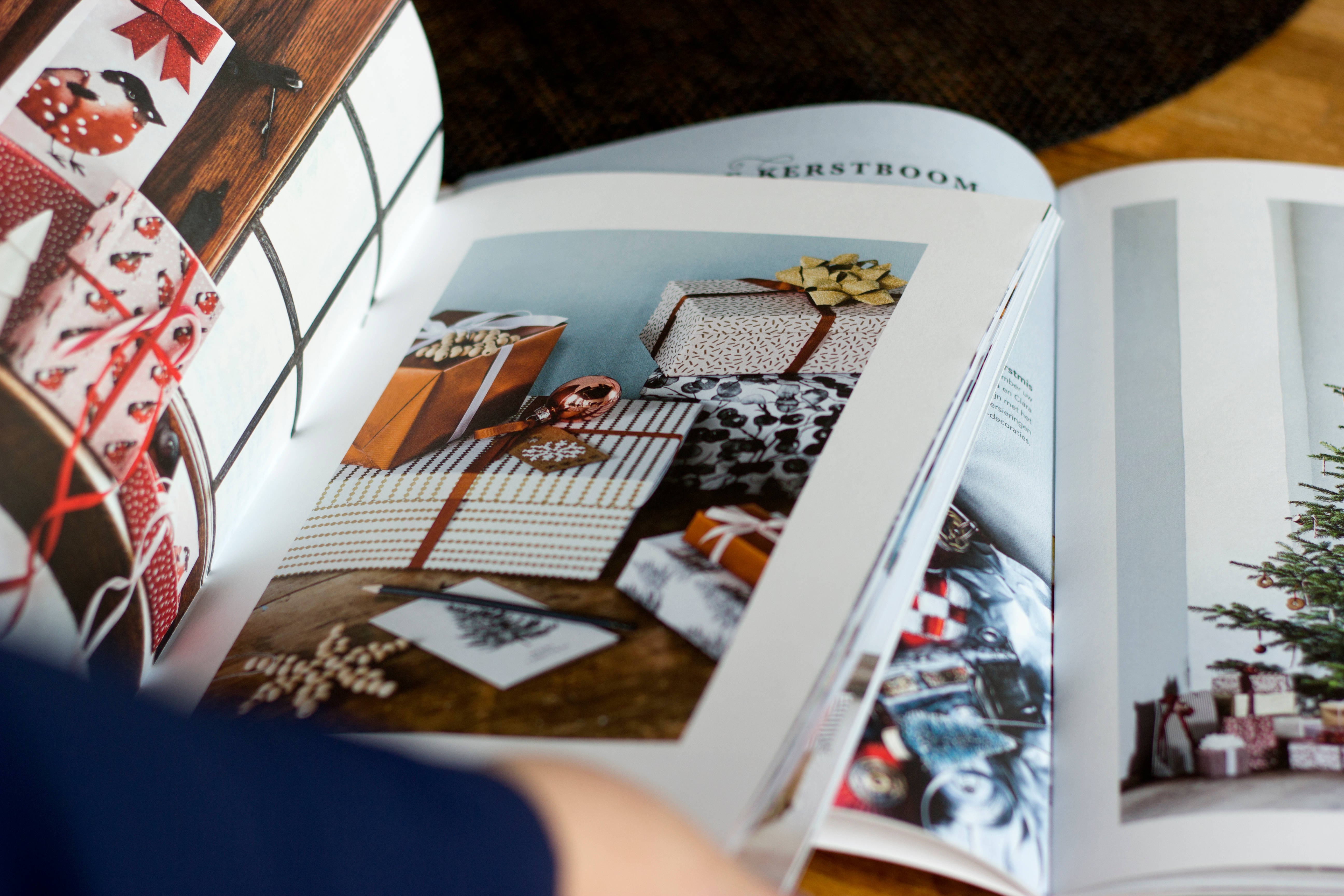Magazine 桌布 壁紙 — 一本打開的雜誌展示節日聖誕禮物包裝設計，包括圖案紙蝴蝶結和松果在木桌上。