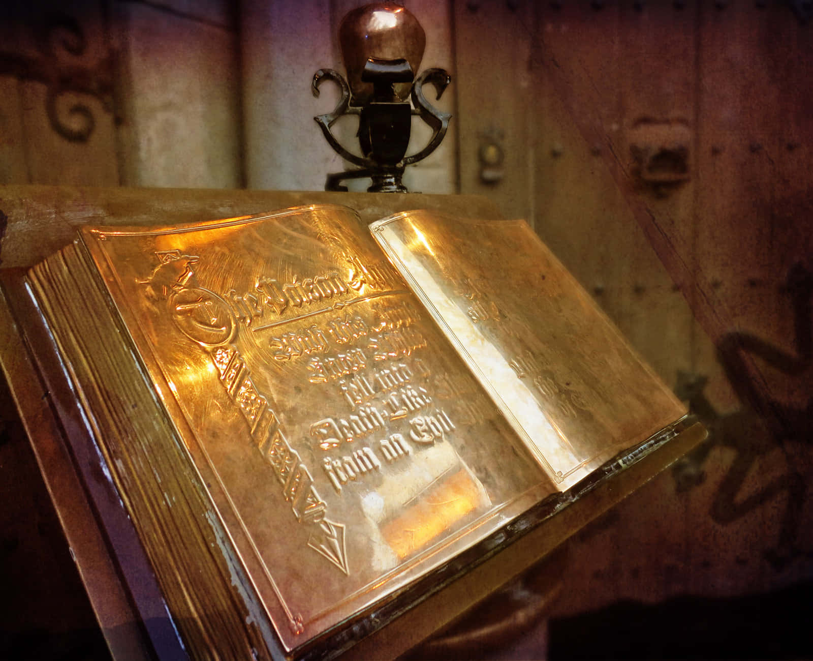 Grimoire 桌布 壁紙 — 一本裝飾華麗的金色書籍，帶有浮雕文字，放在木質表面上，在溫暖的燈光下，附近有一個復古麥克風。