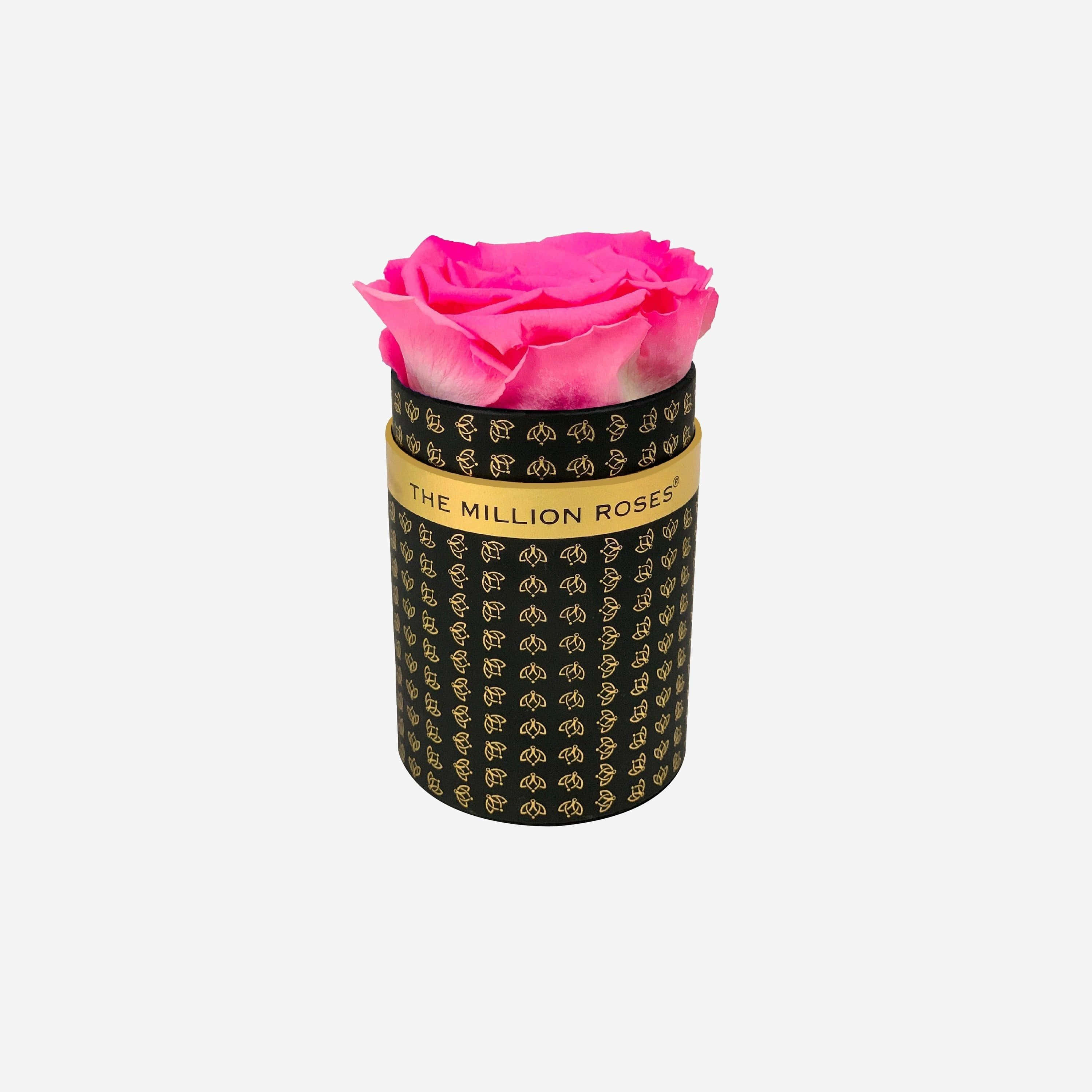 Single Rose 桌布 壁紙 — 一朵充滿活力的粉紅色保鮮玫瑰，從一個飾有金色玫瑰圖案和金色帶子寫著「THE MILLION ROSES」的黑色圓柱形盒子中優雅地綻放。