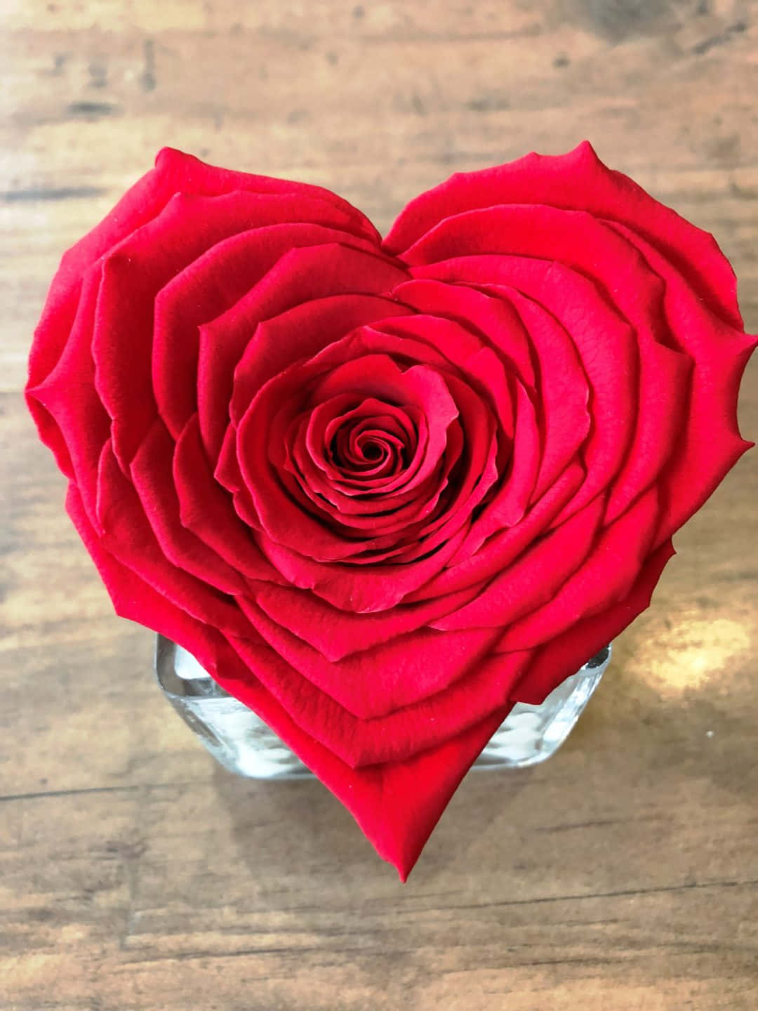 Rose Heart 桌布 壁紙 — 一朵鮮紅的心形玫瑰放在樸實木面上的透明玻璃花瓶中。
