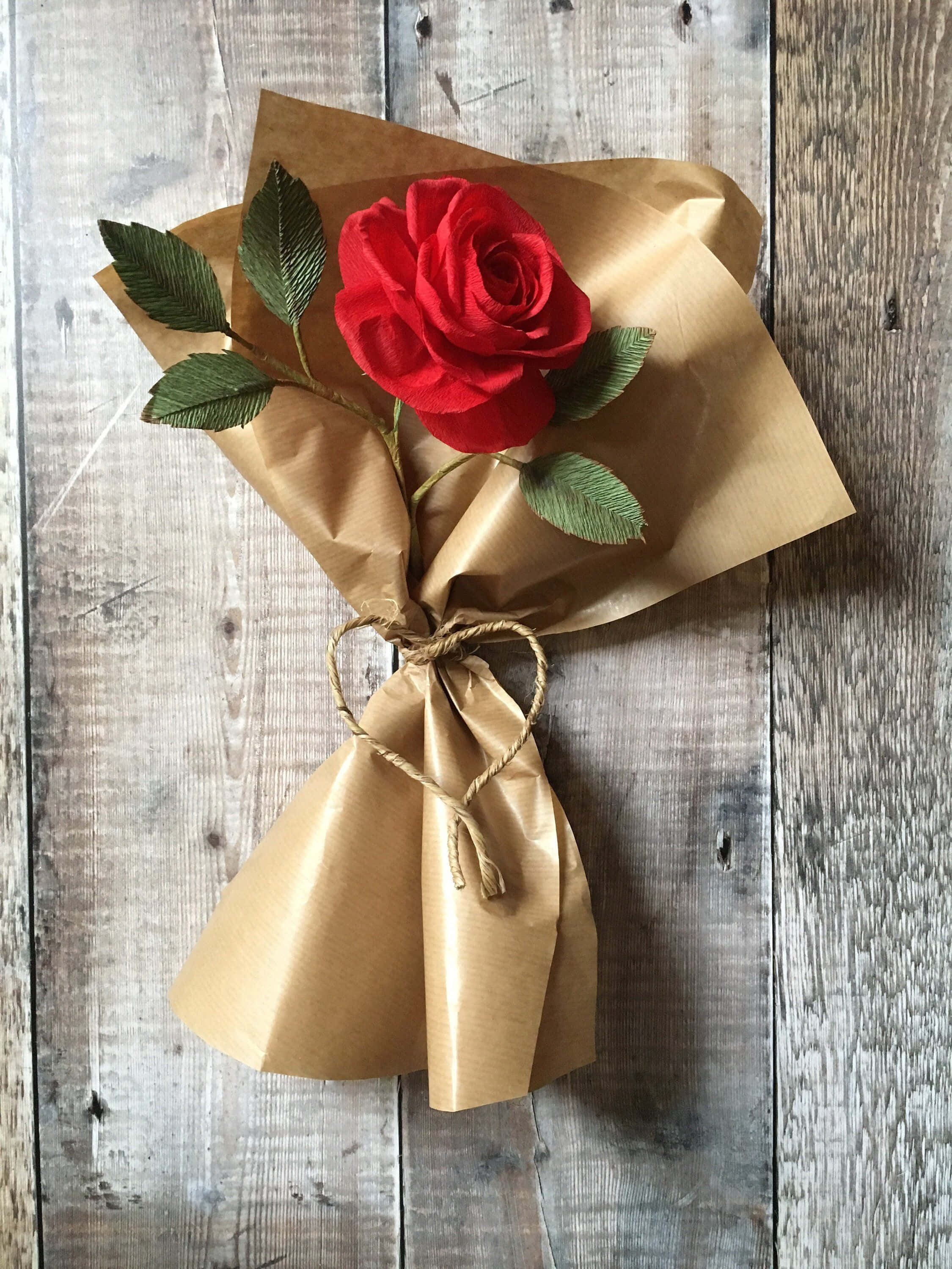 Single Rose 桌布 壁紙 — 一朵鮮紅的玫瑰用牛皮紙和麻繩包裹著，放在風化的灰色木板上。