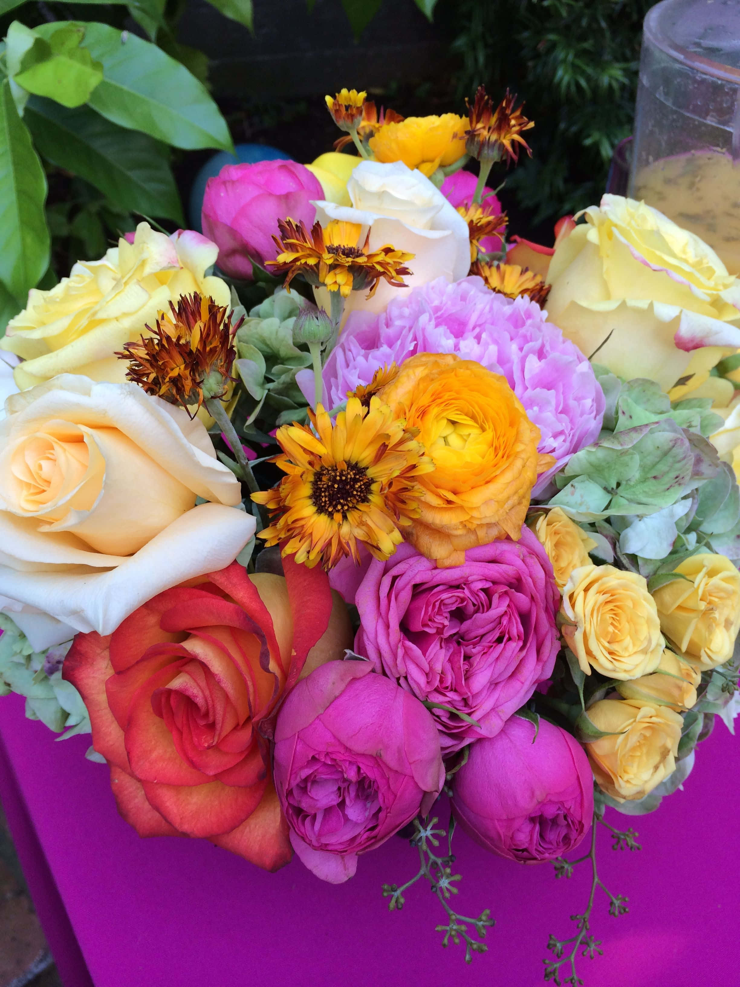 Flower Bouquet 桌布 壁紙 — 一束充滿活力的玫瑰花、牡丹花和向日葵，以粉紅、黃色和橙色的花朵綻放在鮮豔的紫色表面上。