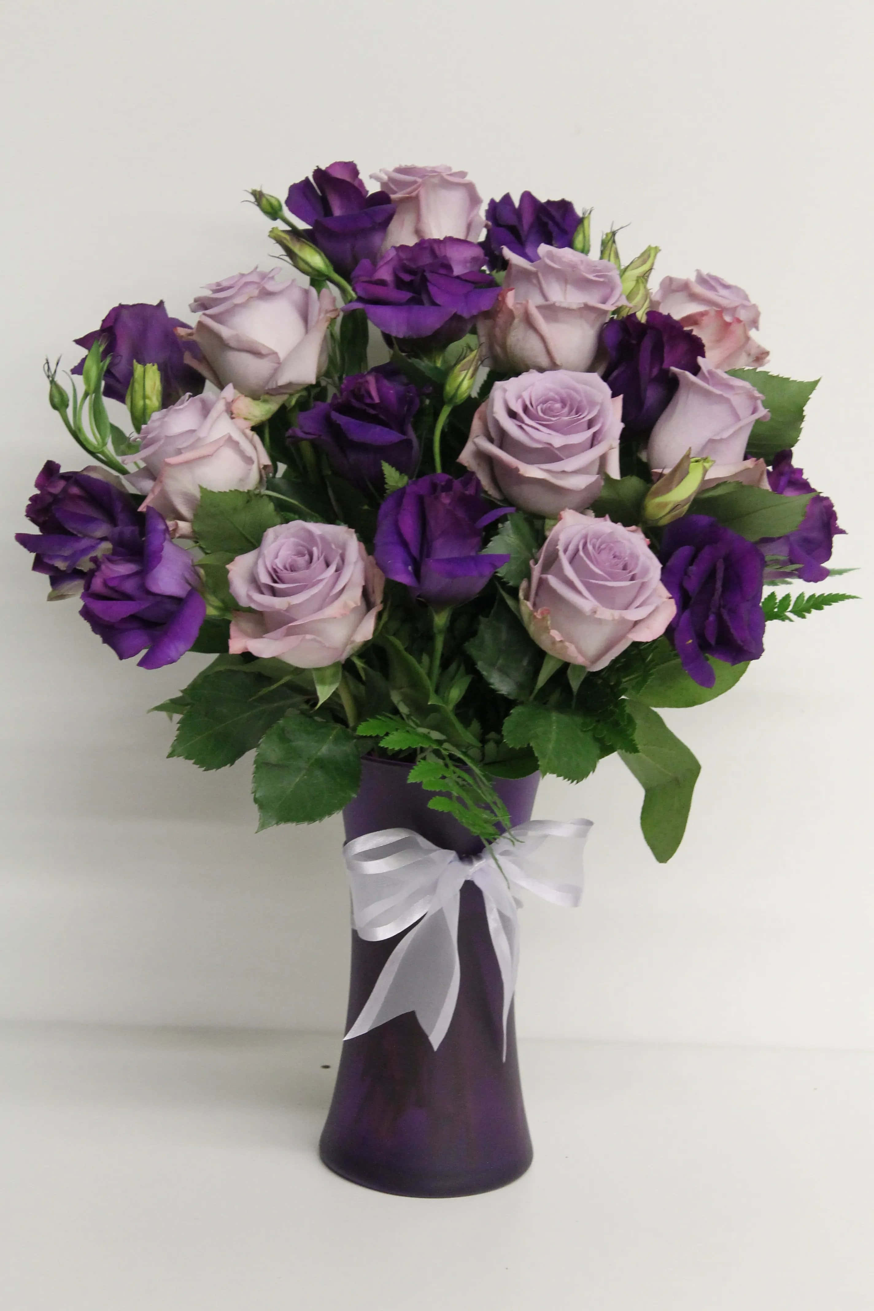 Flower Bouquet 桌布 壁紙 — 一束充滿活力的紫色和薰衣草玫瑰及洋桔梗，放在相配的紫色花瓶裡，繫著白色蝴蝶結，背景是純白色。
