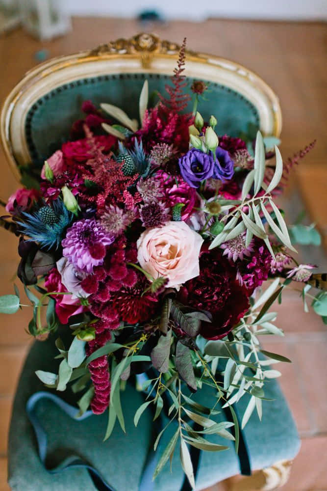 Roses Wedding 桌布 壁紙 — 一束深紅、紫和粉紅色的茂盛花束放在一張帶有金色飾邊的復古綠色軟墊椅子上。