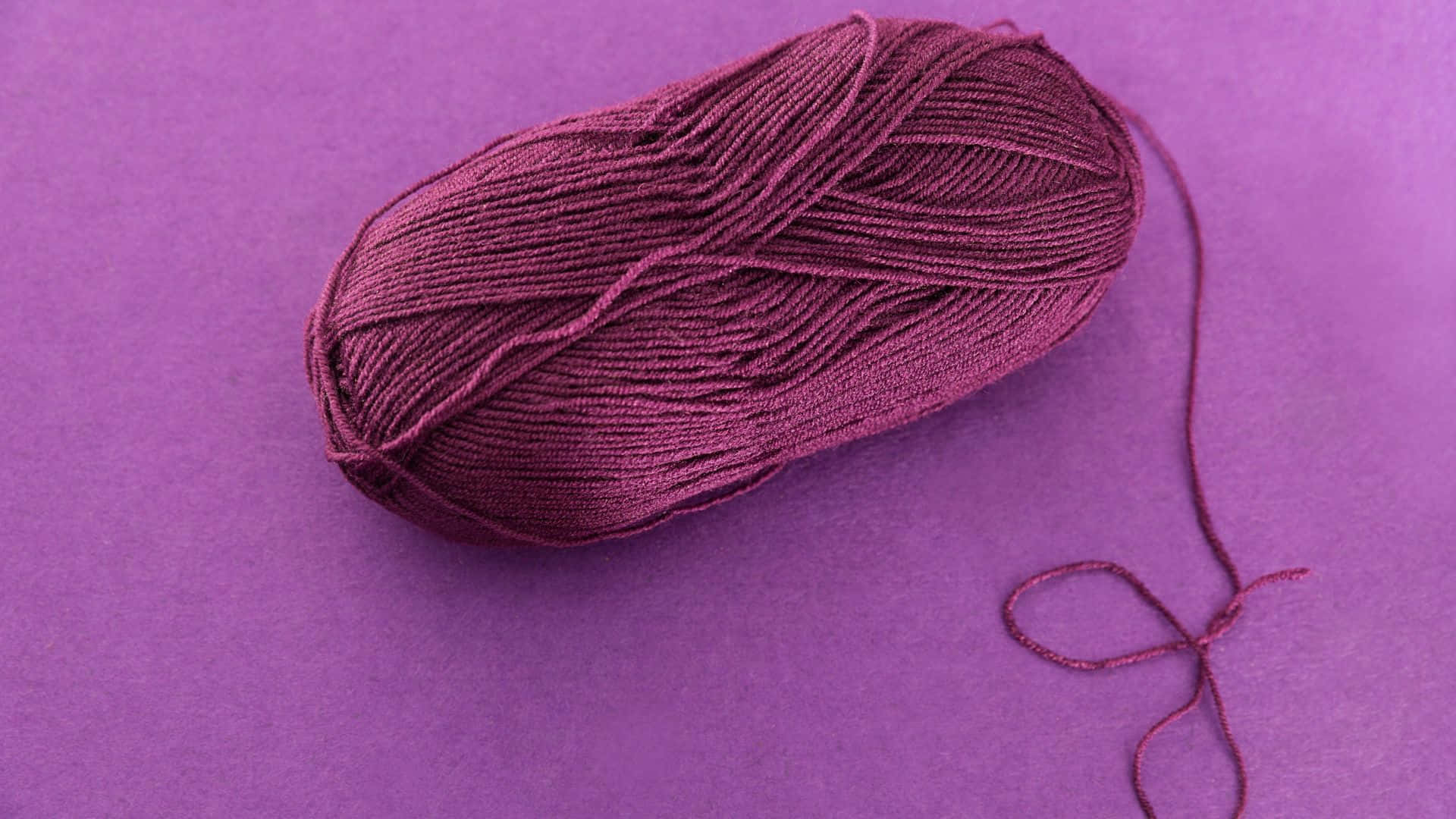 Purple Wool 桌布 壁紙 — 一束深酒紅色毛線放在純紫色背景上，鬆散的線尾垂落。