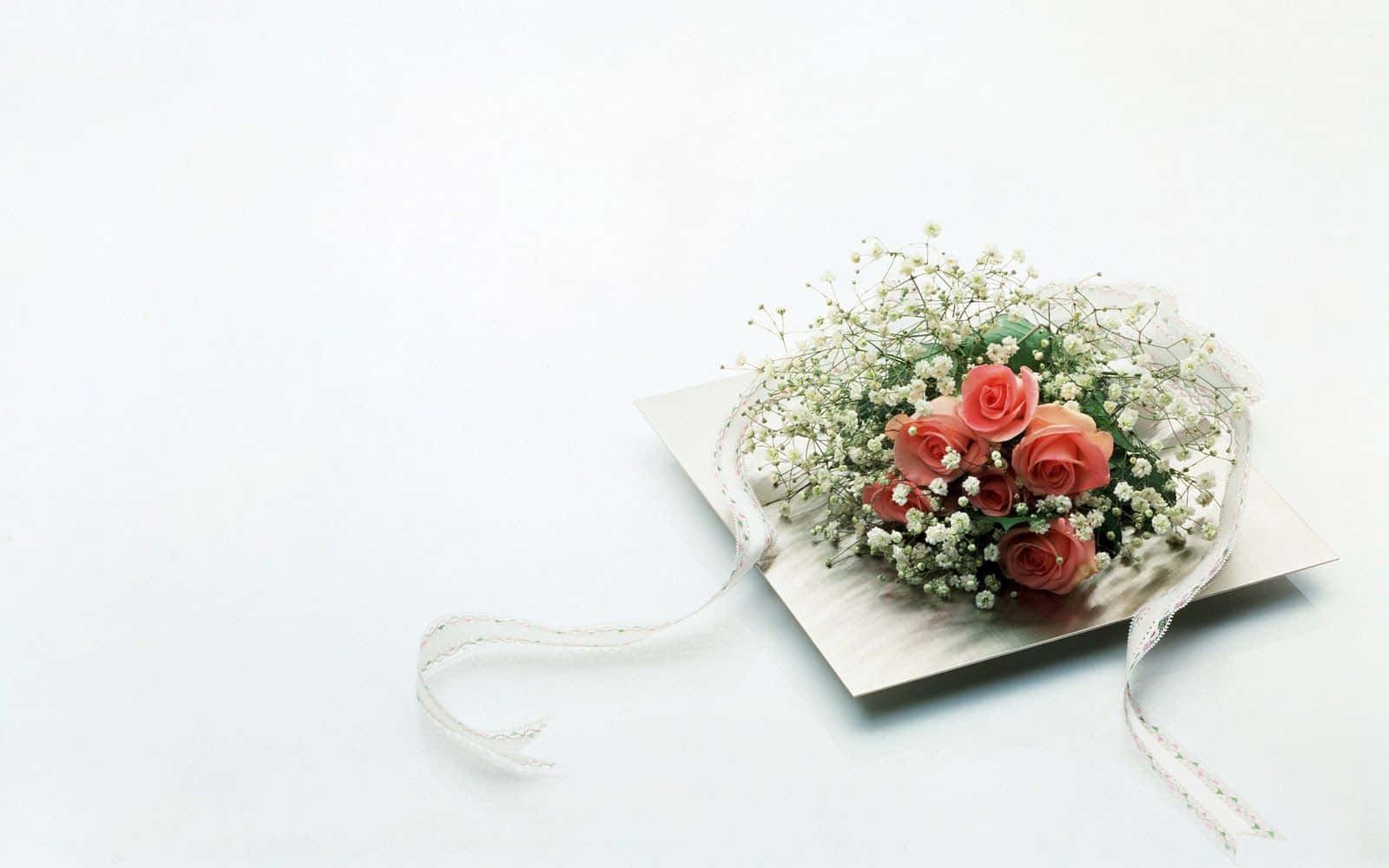 Wedding Flowers 桌布 壁紙 — 一束用白色絲帶綁著的珊瑚玫瑰和滿天星，放在純白背景的銀色卡片上。