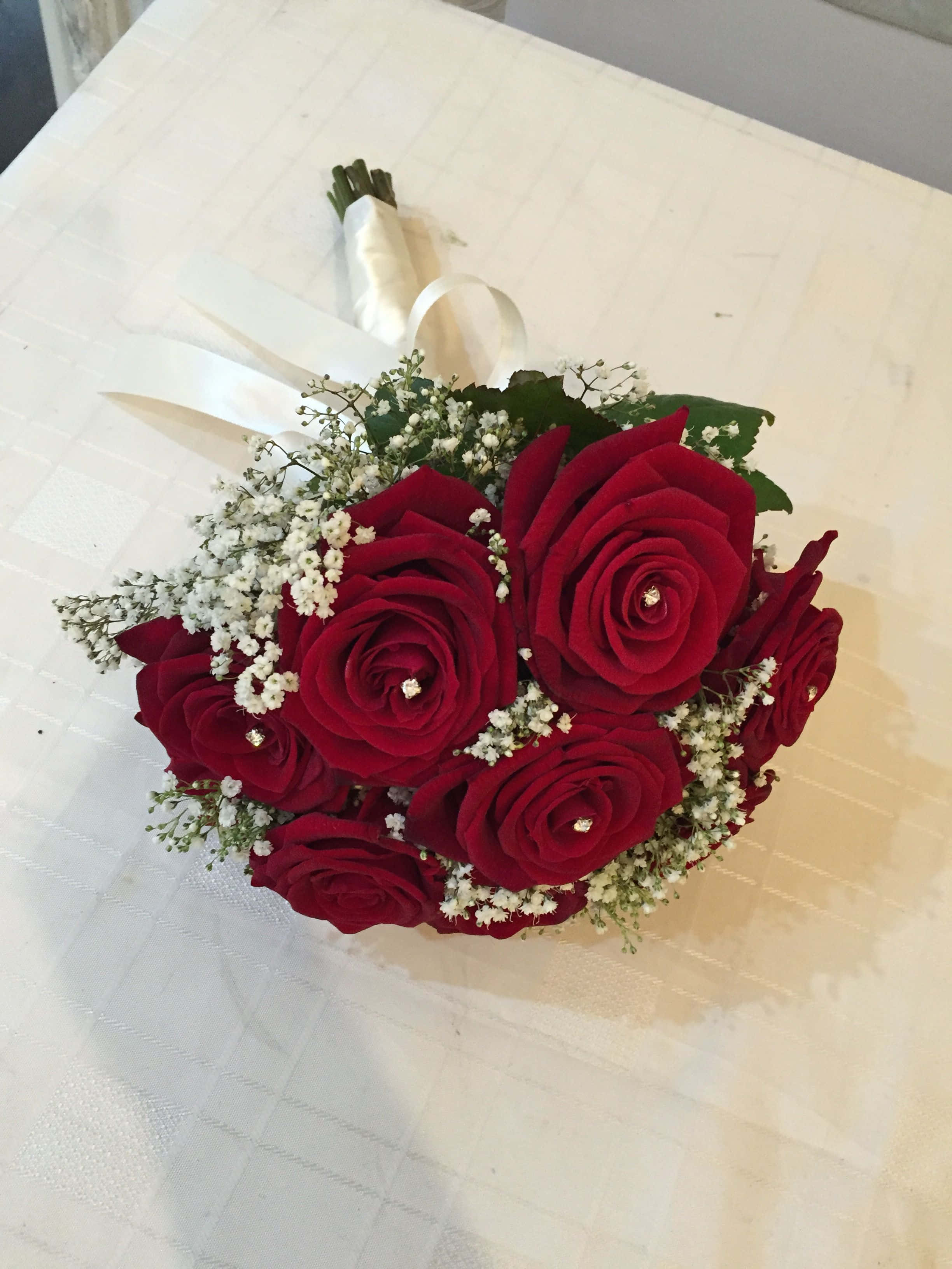Roses Wedding 桌布 壁紙 — 一束由深紅玫瑰和滿天星組成的豐盛花束，用白色絲帶繫著，放在白色紋理桌布上。