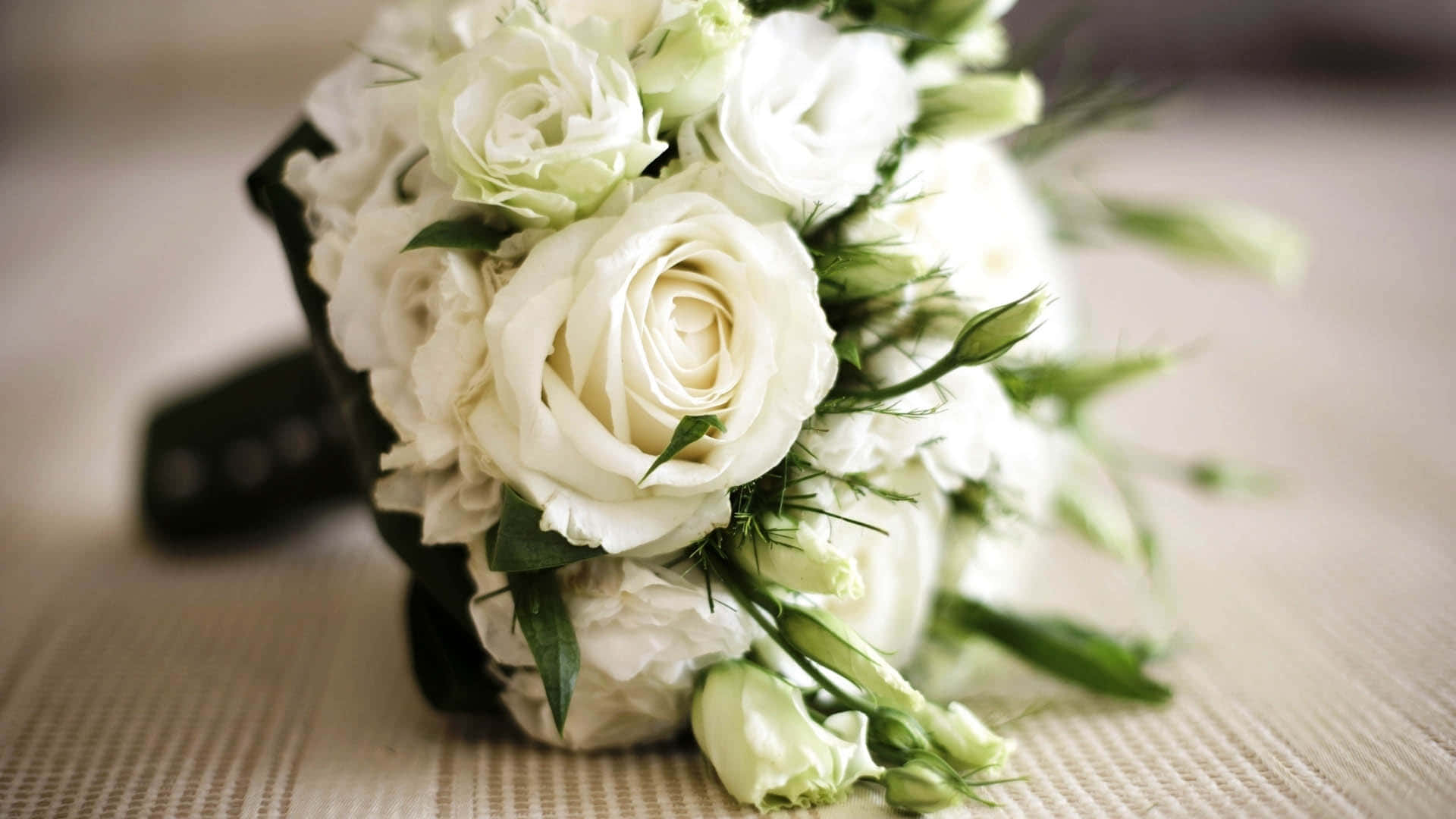 Wedding Bouquet 桌布 壁紙 — 一束精緻白玫瑰的特寫，帶有綠色莖和花蕾，放置在紋理米色表面上。