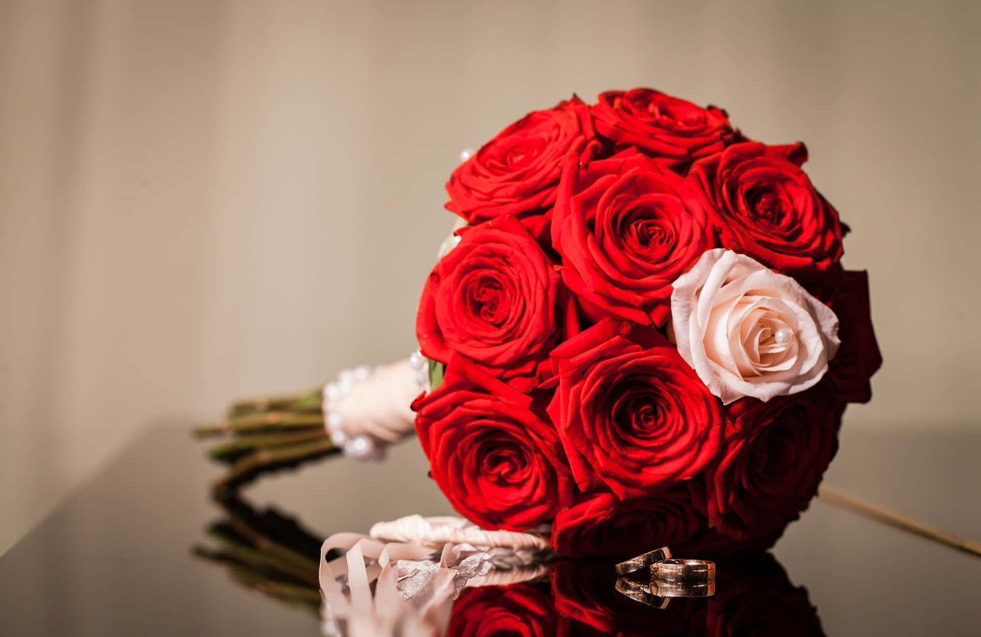 紅玫瑰和淡粉玫瑰束，結婚戒指在反光表面