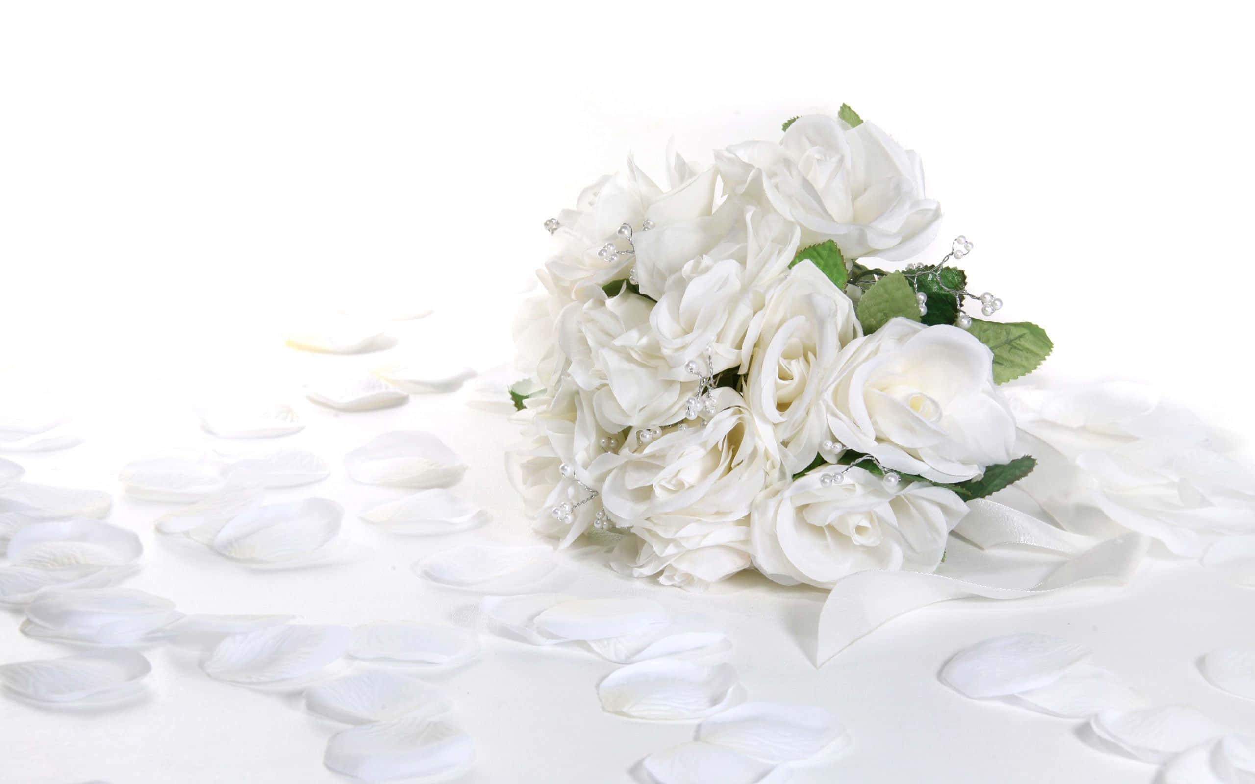 Wedding Flowers 桌布 壁紙 — 一束純潔的白玫瑰，花瓣散落，放在純白色的表面上，點綴著精緻的綠葉和閃閃發光的珠子。