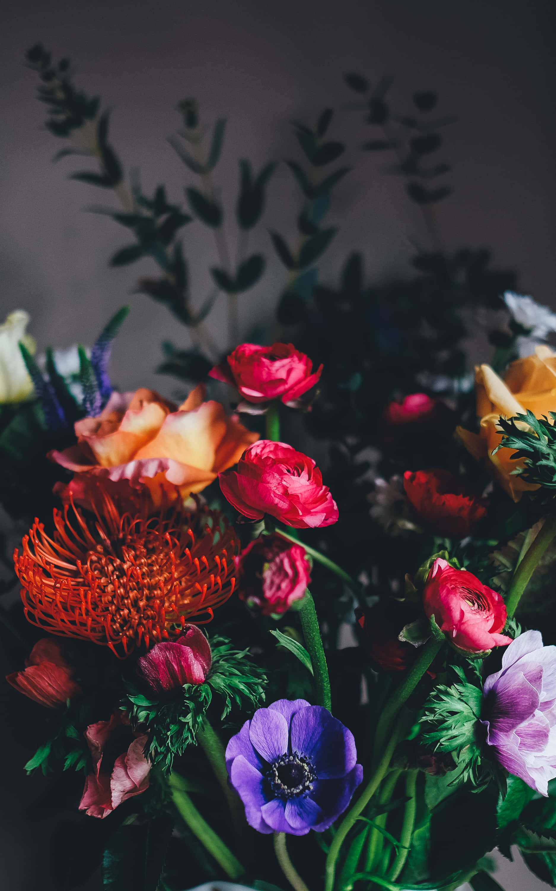 Flower Phone 桌布 壁紙 — 一束色彩鮮豔的紅、粉紅、橙和紫色花朵，配以綠色葉子，襯托在深色柔和背景上。