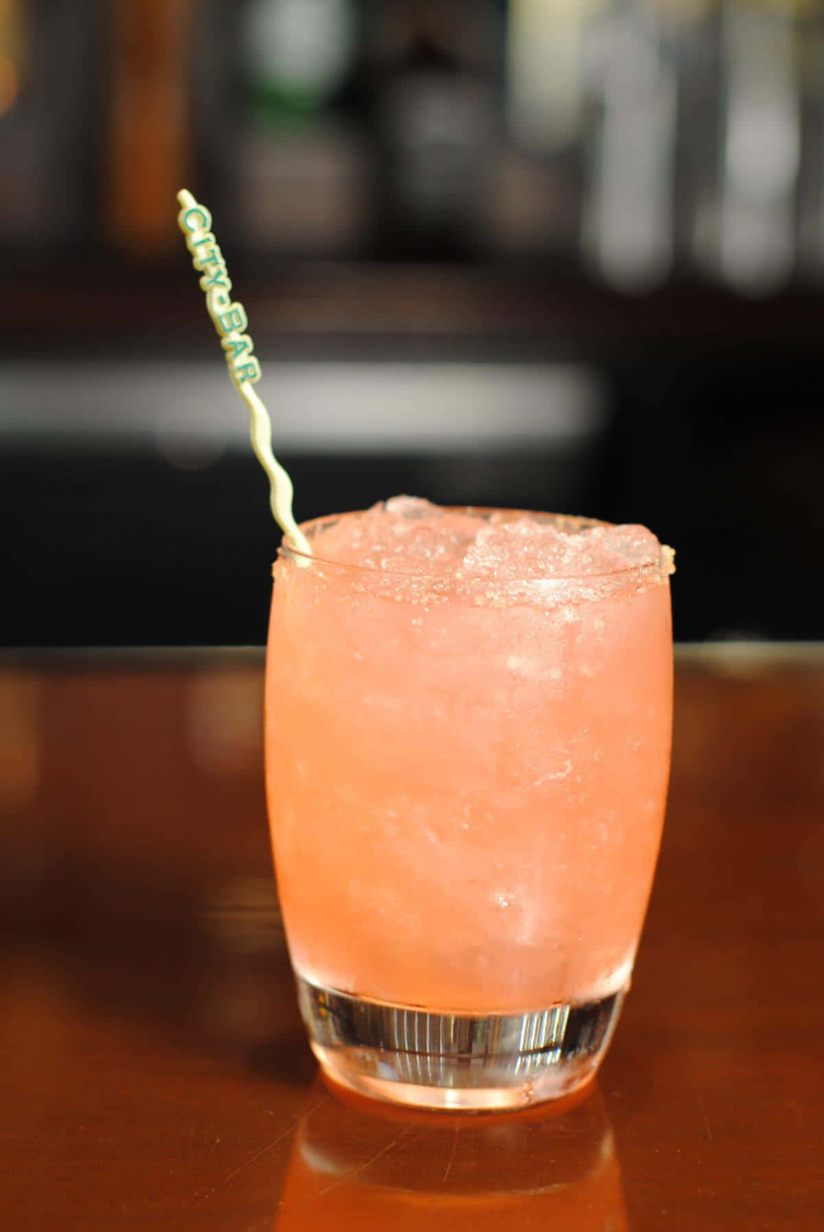 Beautiful Drink 桌布 壁紙 — 一杯充滿活力的粉紅色冰凍雞尾酒，帶有糖邊和品牌吸管，放在深色木質吧檯上。