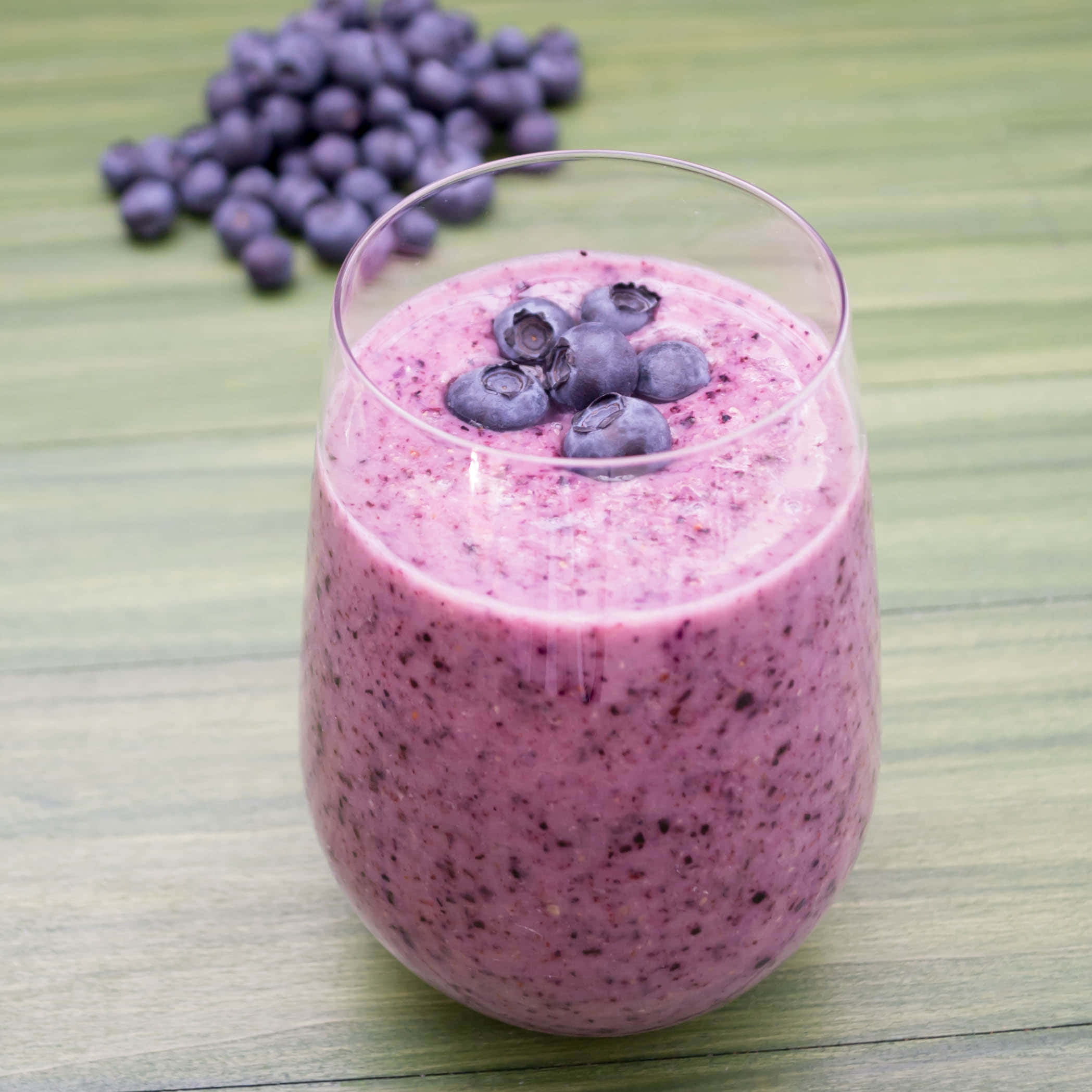 Blueberry Smoothie 桌布 壁紙 — 一杯充滿活力的紫色藍莓冰沙，上面放上新鮮藍莓，放在綠色木質表面上。