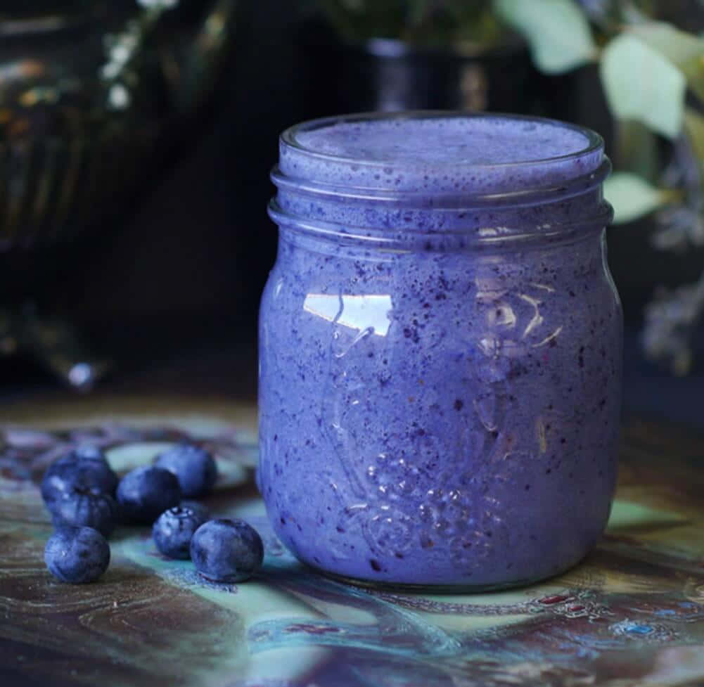 Blueberry Smoothie 桌布 壁紙 — 一杯充滿活力的紫色藍莓冰沙放在玻璃罐中，旁邊是新鮮藍莓，置於色彩繽紛的圖案表面上。