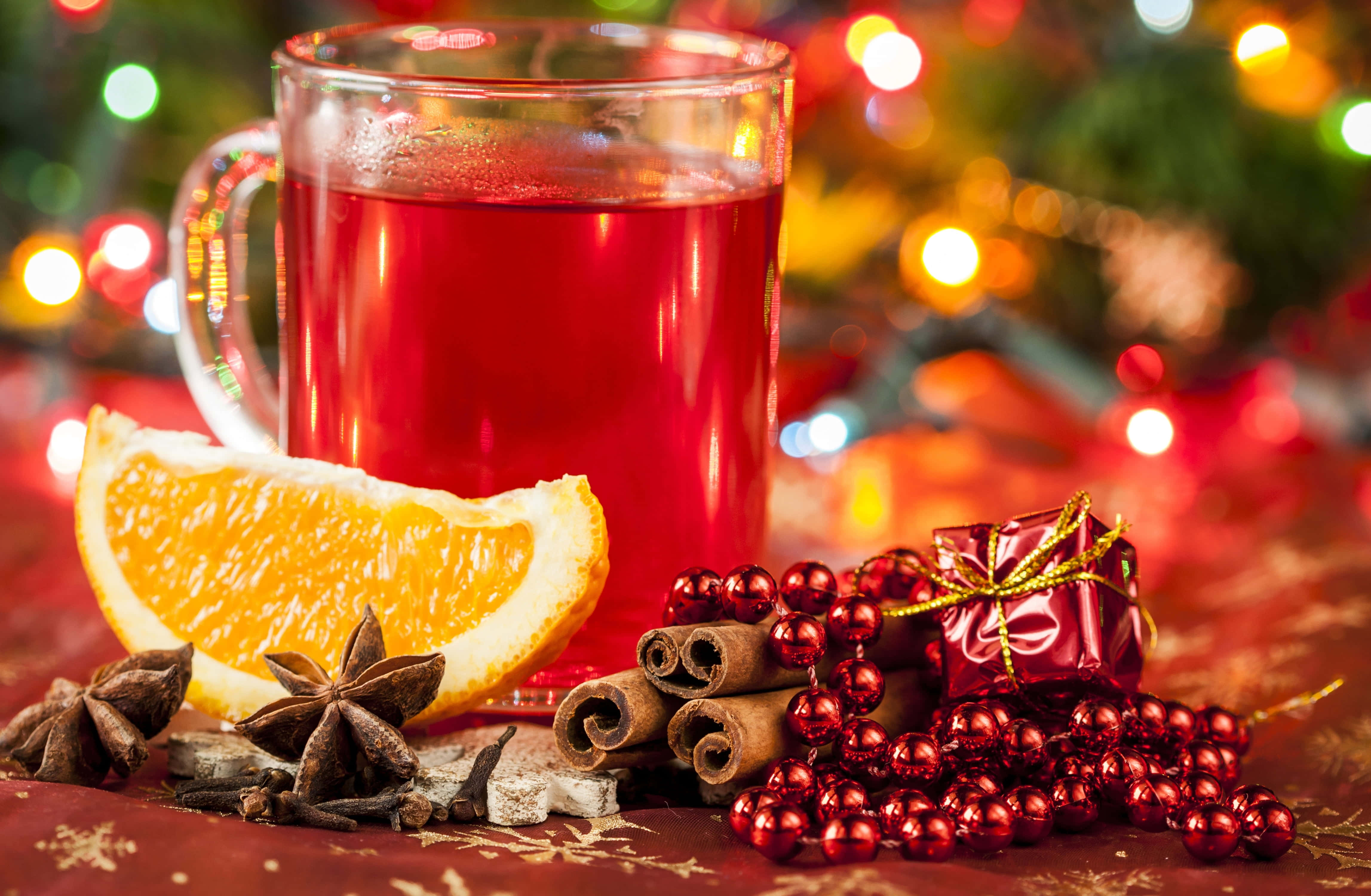 Mulled Wine 桌布 壁紙 — 一杯冒煙的紅酒香料熱飲，周圍有橙片、肉桂棒和八角，背景是節日散景效果。